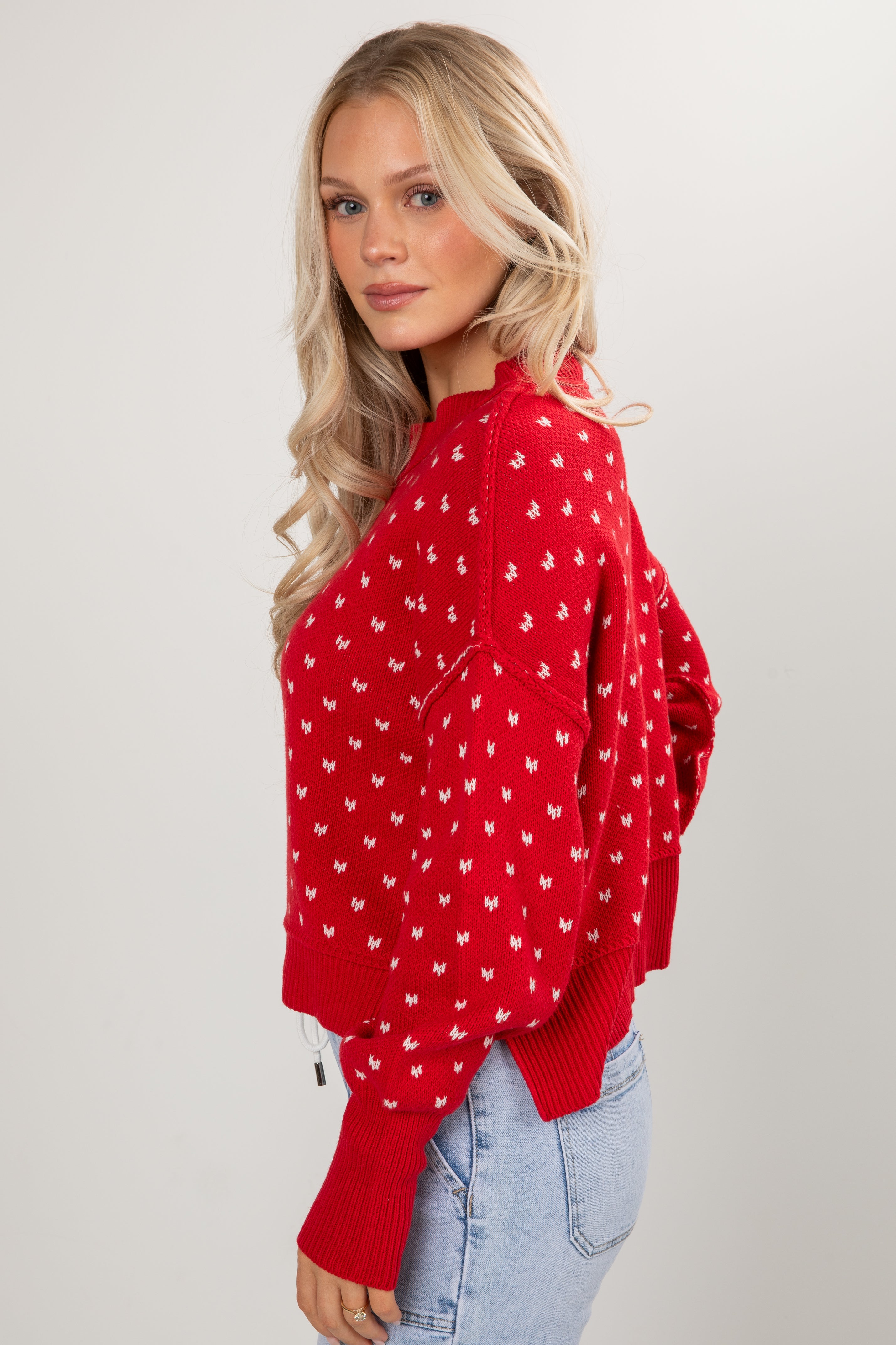 Woman wearing a red sweater with white patterns on a plain background