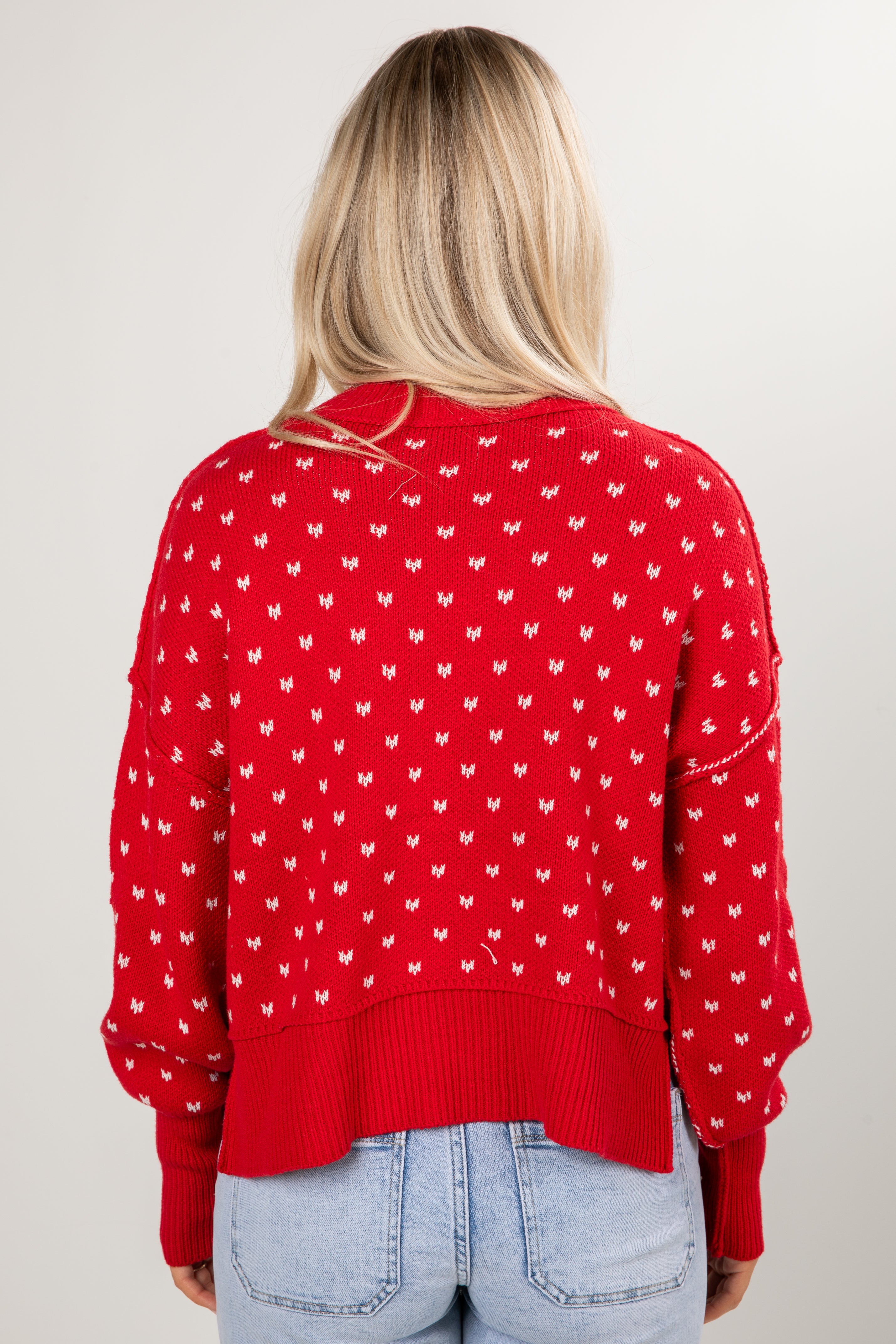 Person wearing a red sweater with white patterns on a plain background