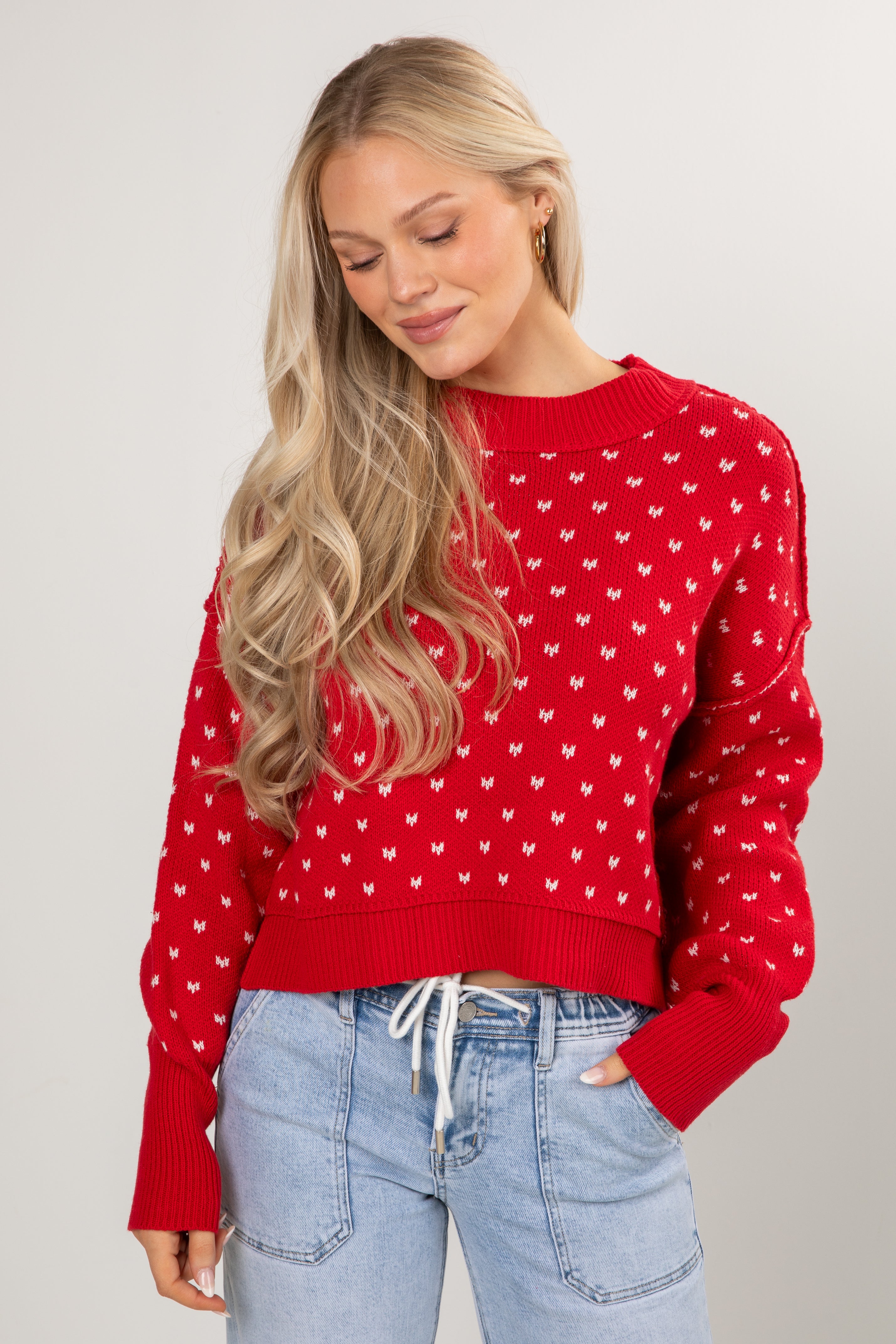 Woman wearing a red sweater with white patterns and light blue jeans on a plain background