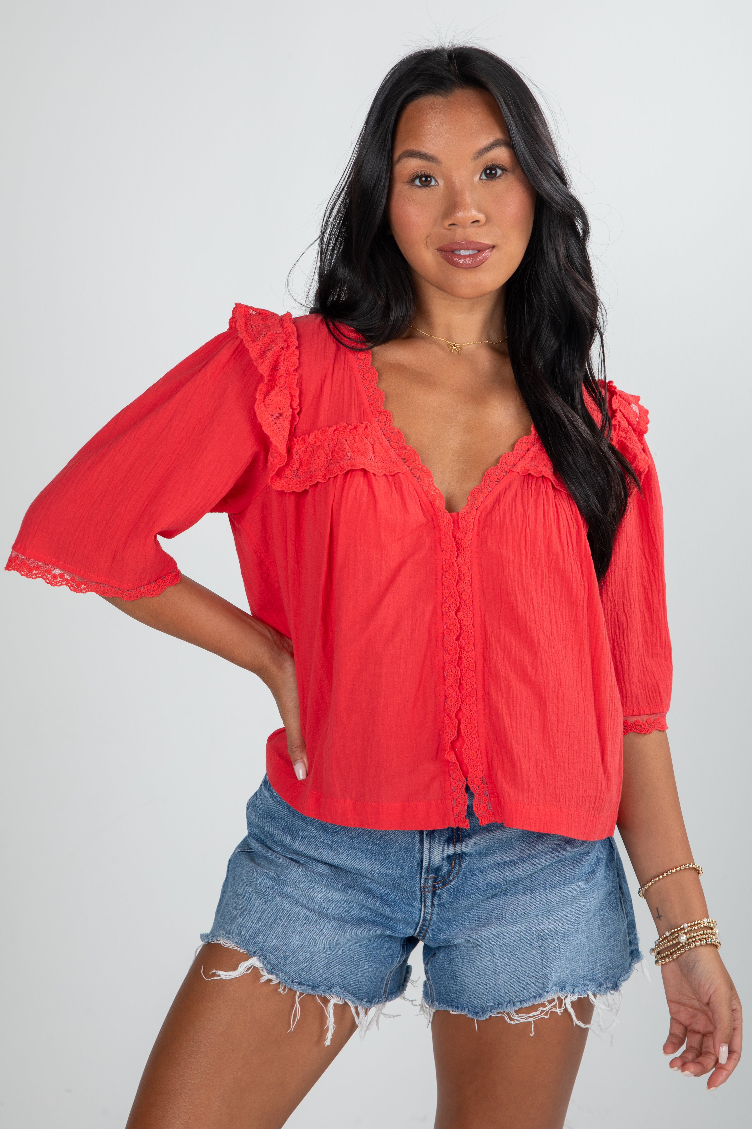 Woman wearing a red blouse with ruffled sleeves and denim shorts on a white background