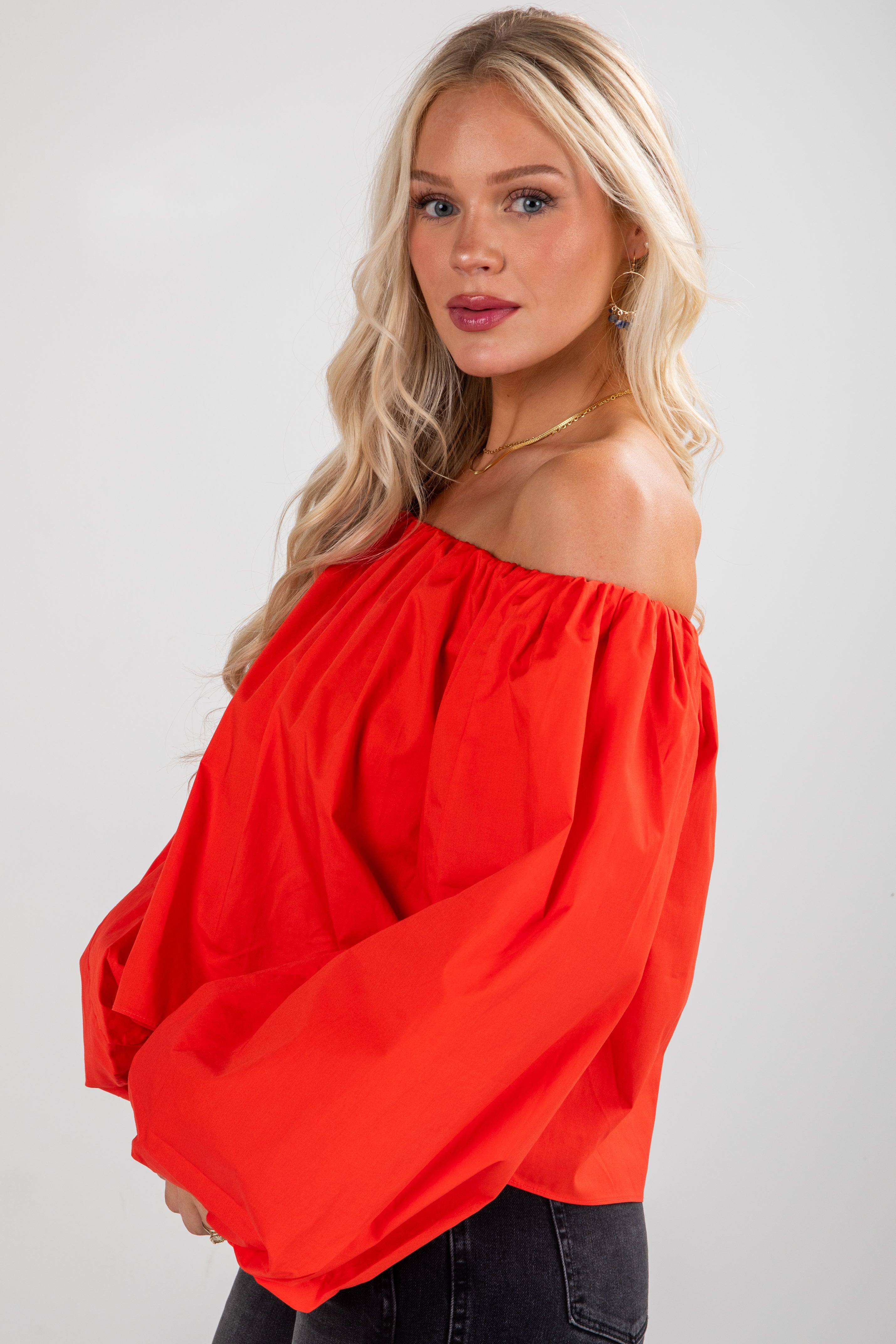 Woman wearing a red off-shoulder blouse against a white background
