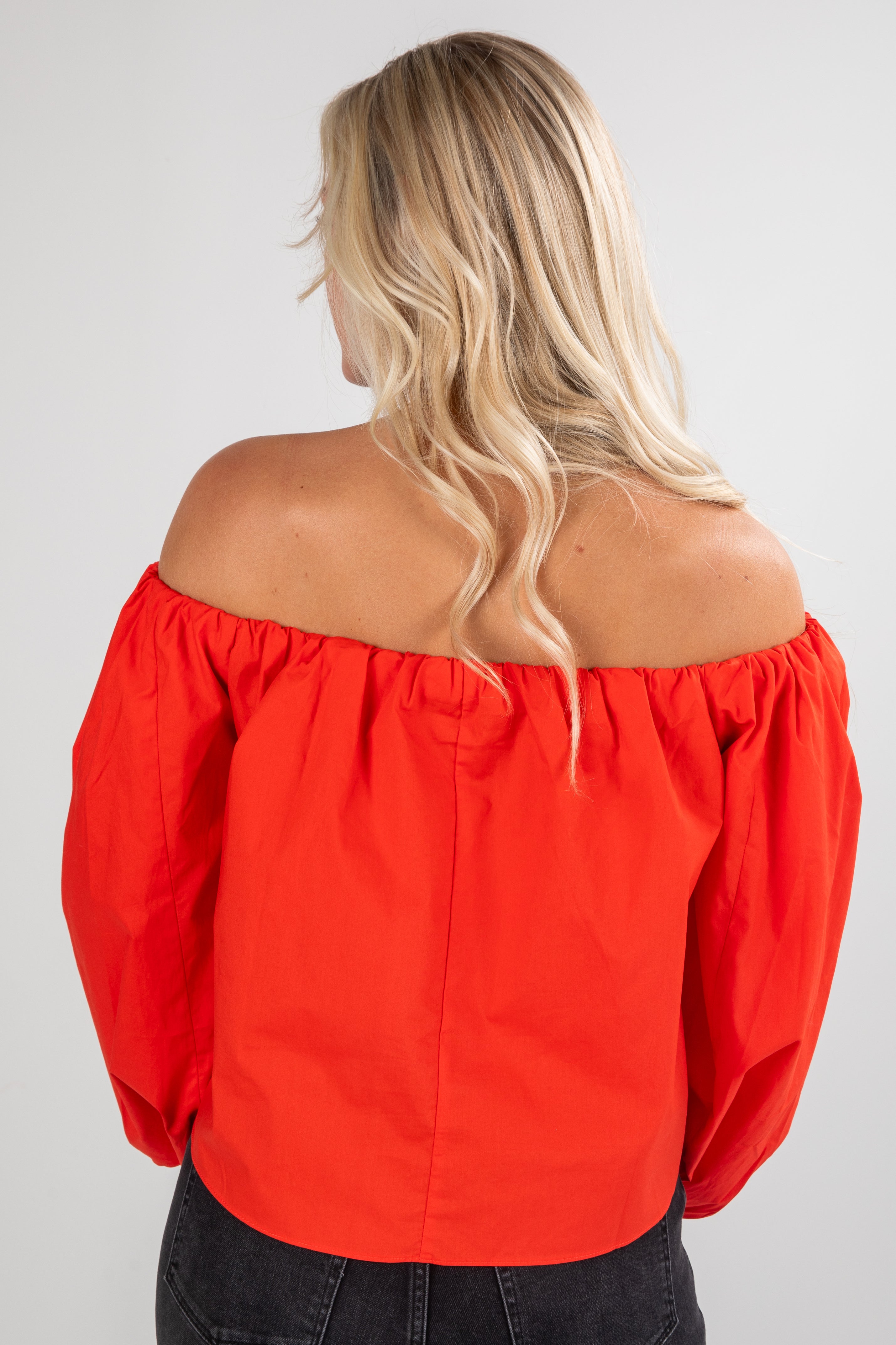 Person wearing a red off-shoulder top on a plain background