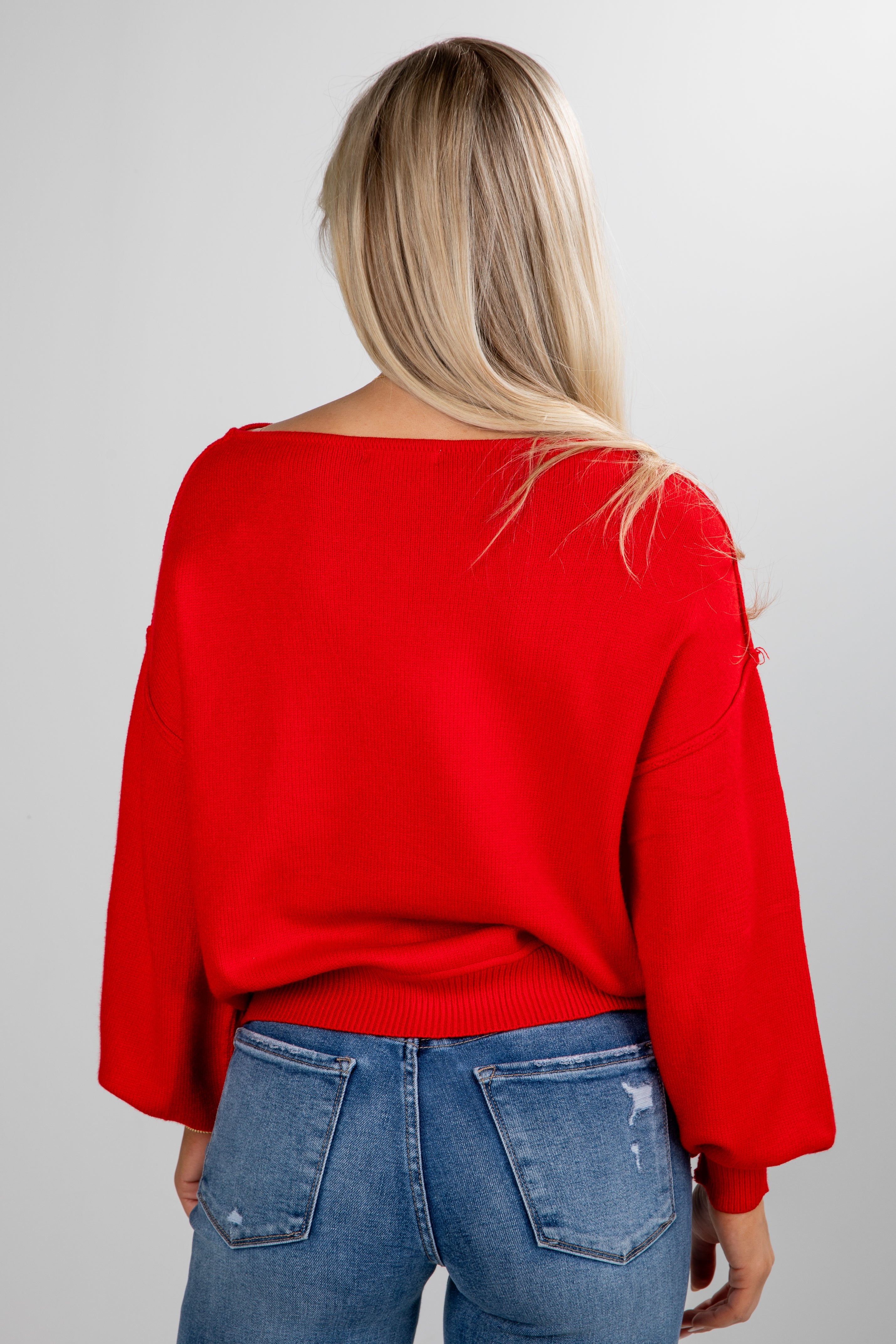 Person wearing a red sweater and blue jeans on a plain background