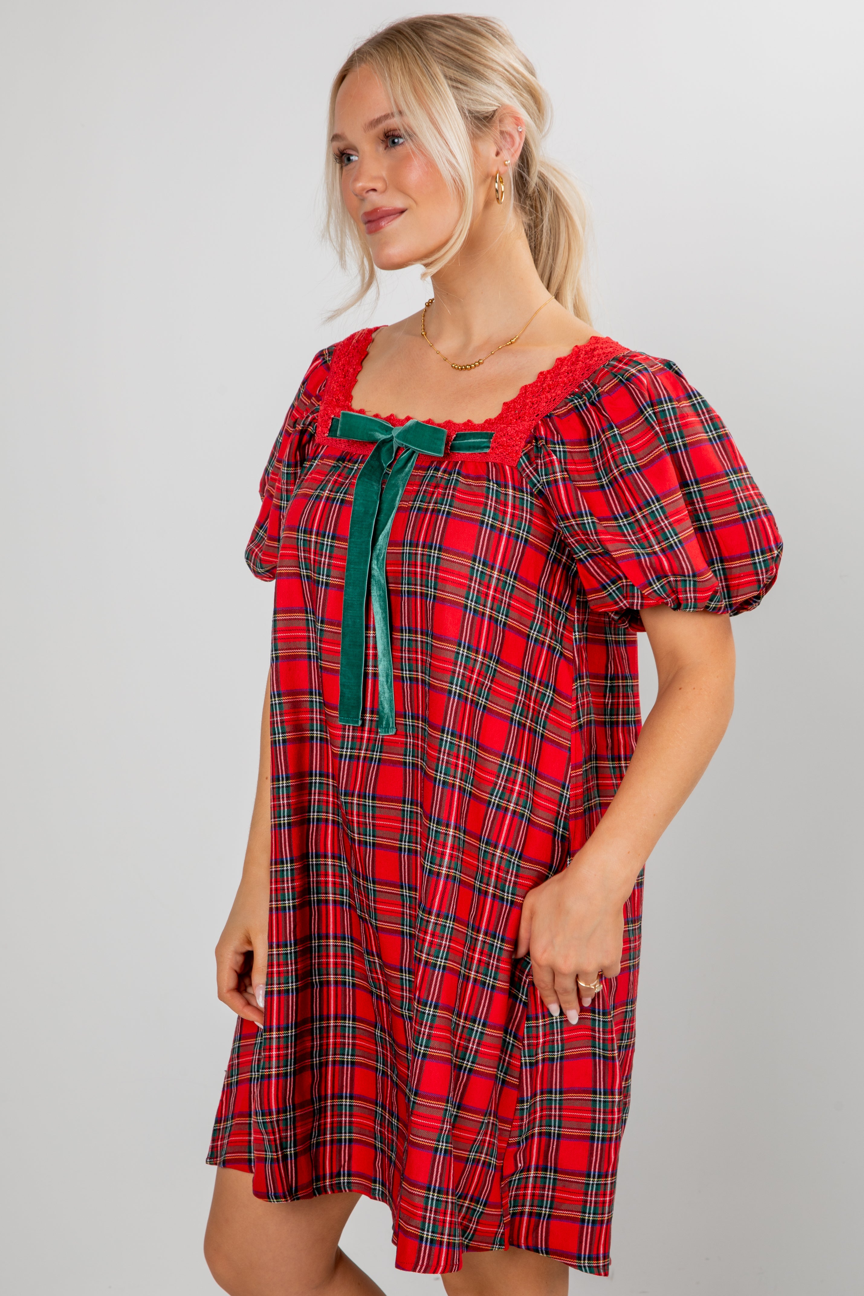 Woman wearing a red plaid dress with green accents on a plain background