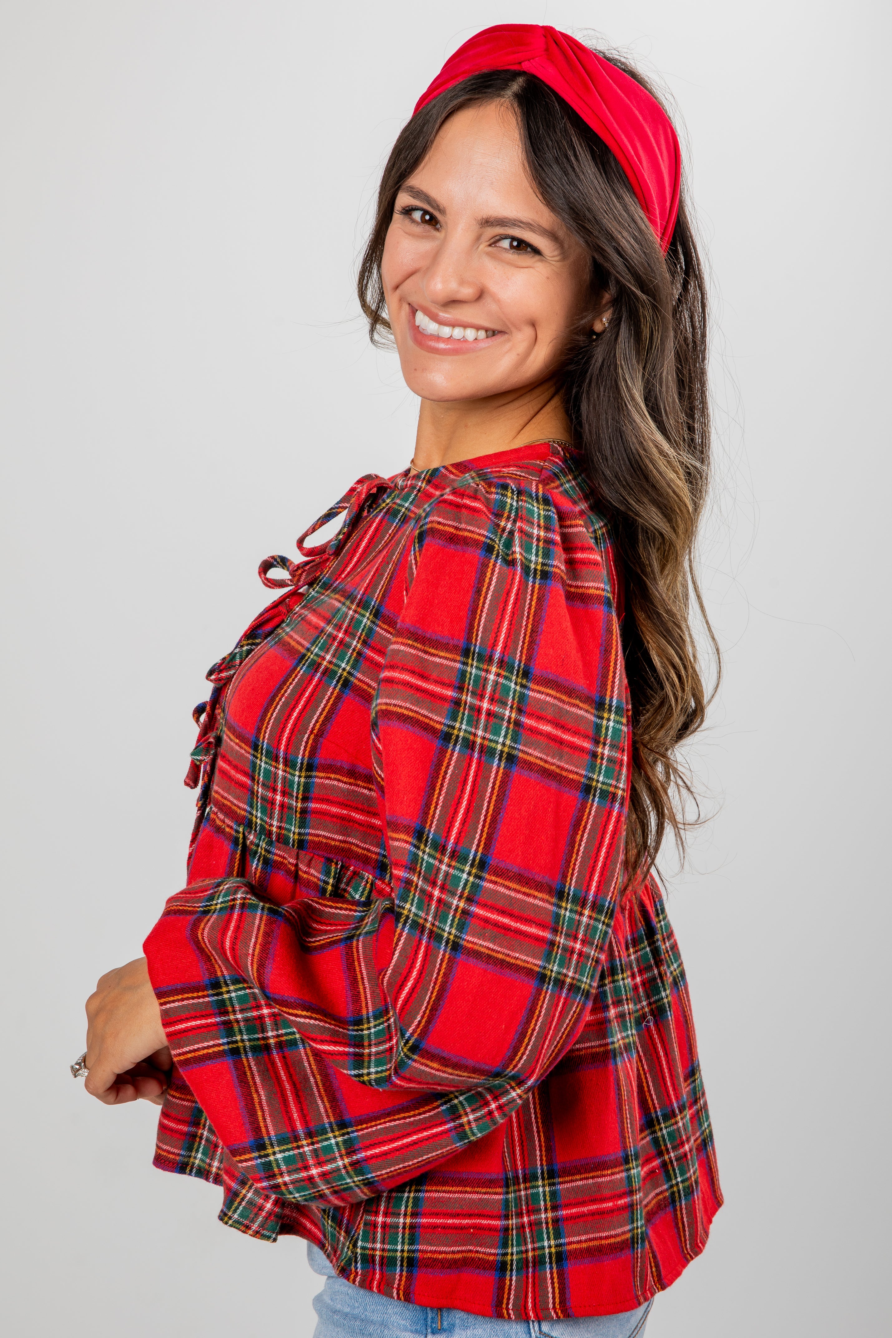 Woman wearing a red plaid shirt and headband against a gray background