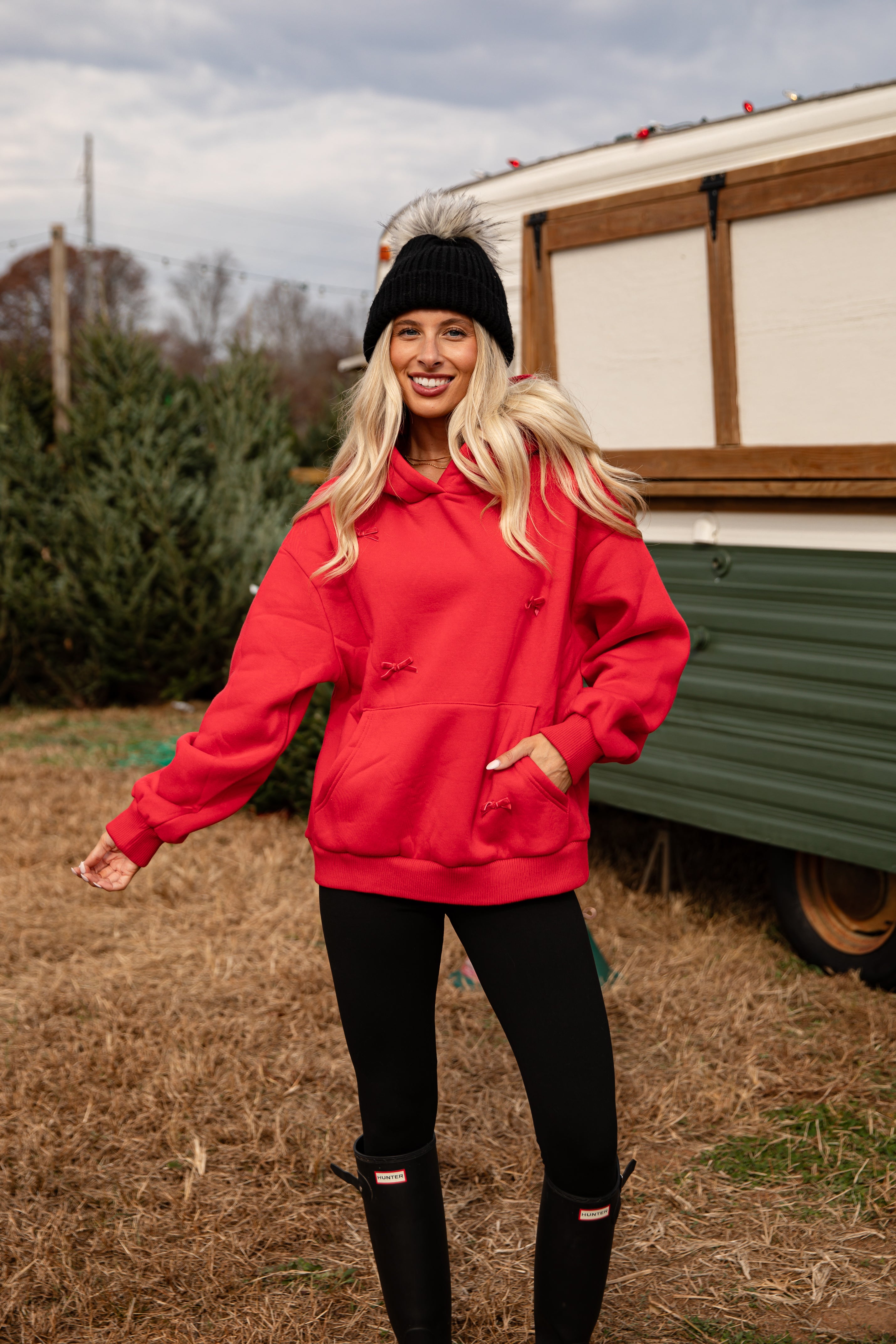 Woman wearing a red sweatshirt and black pants standing in front of a vintage camper.