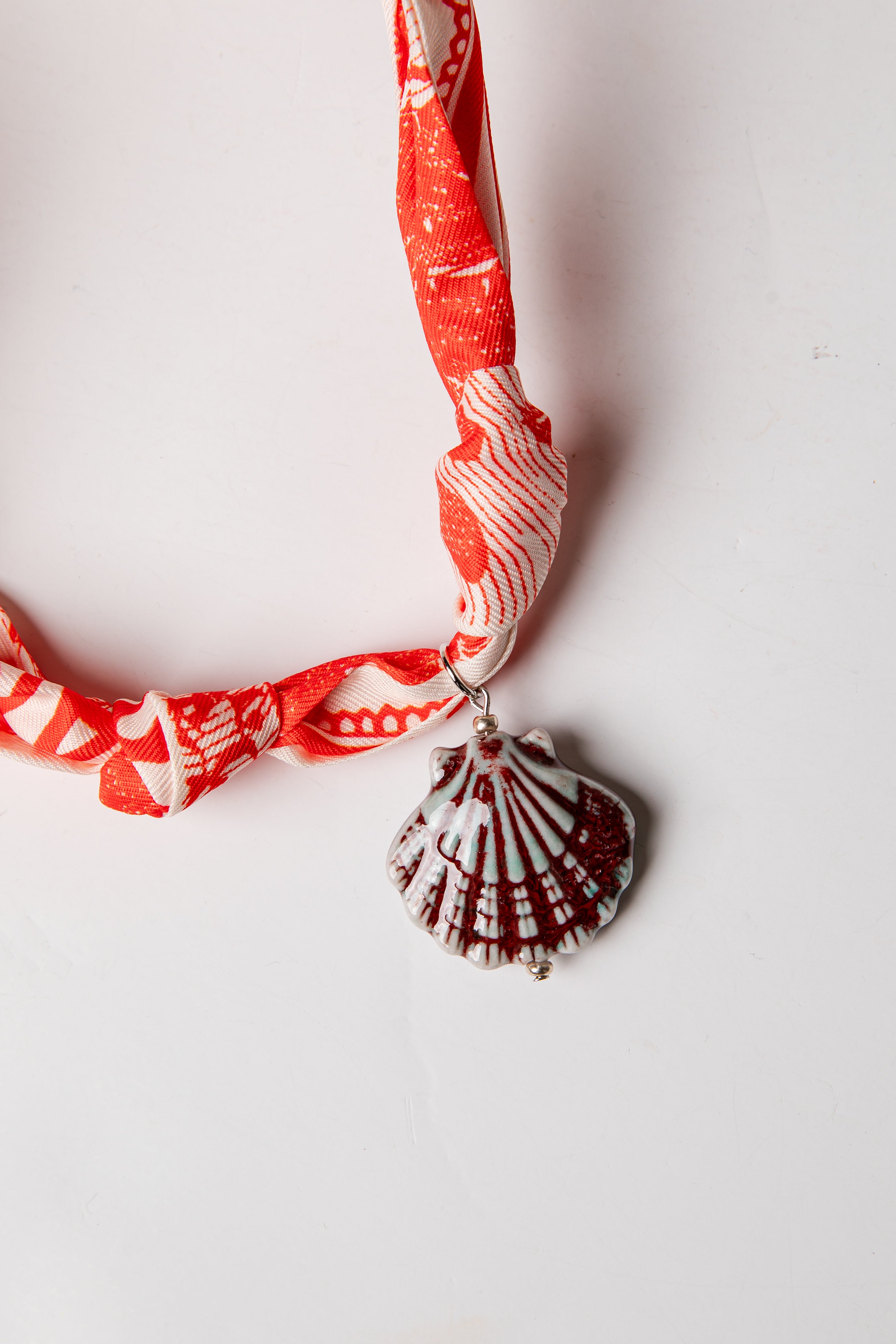 Necklace with a red and white patterned fabric strap and a shell pendant on a light background
