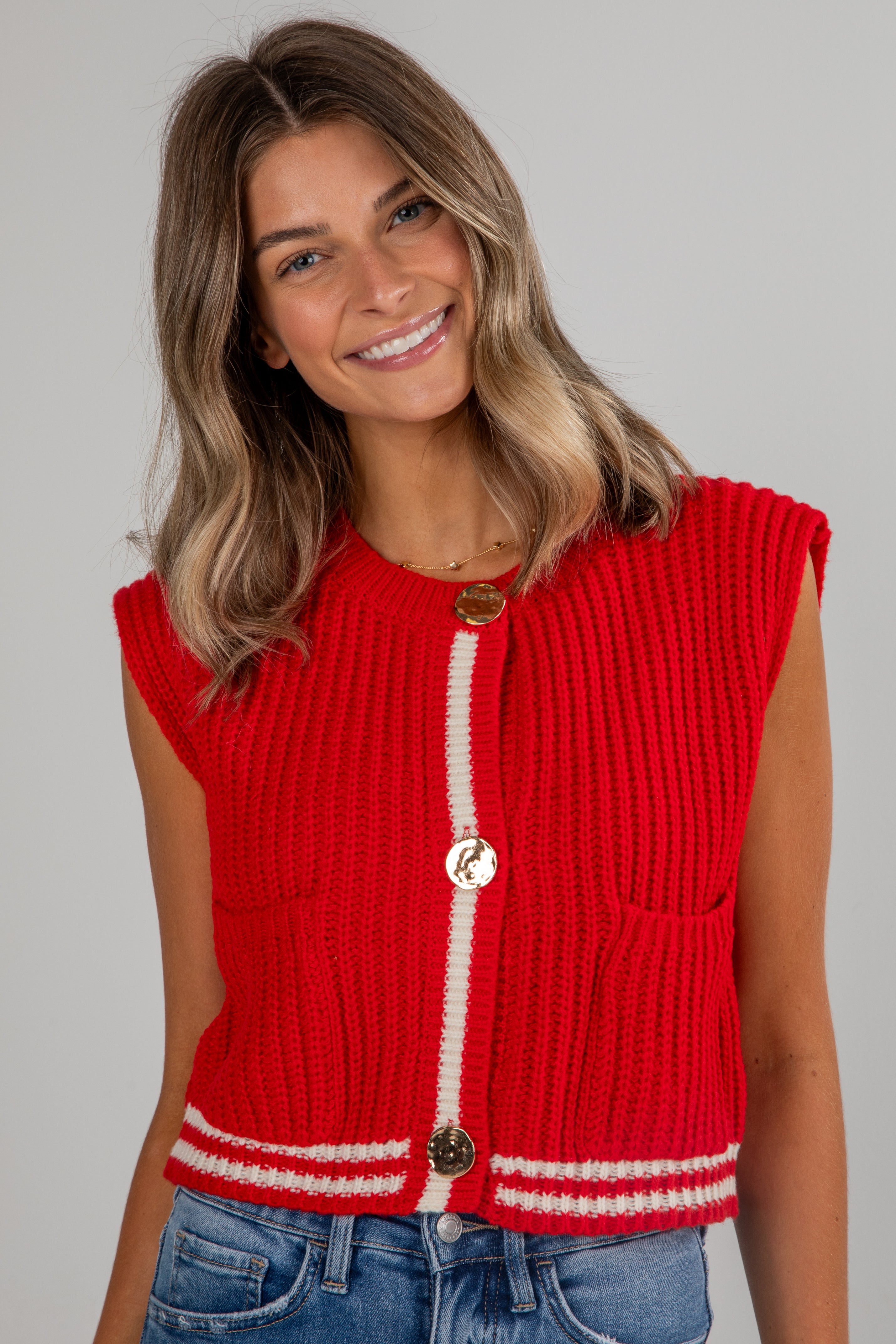 Woman wearing a red knitted vest with white trim on a gray background