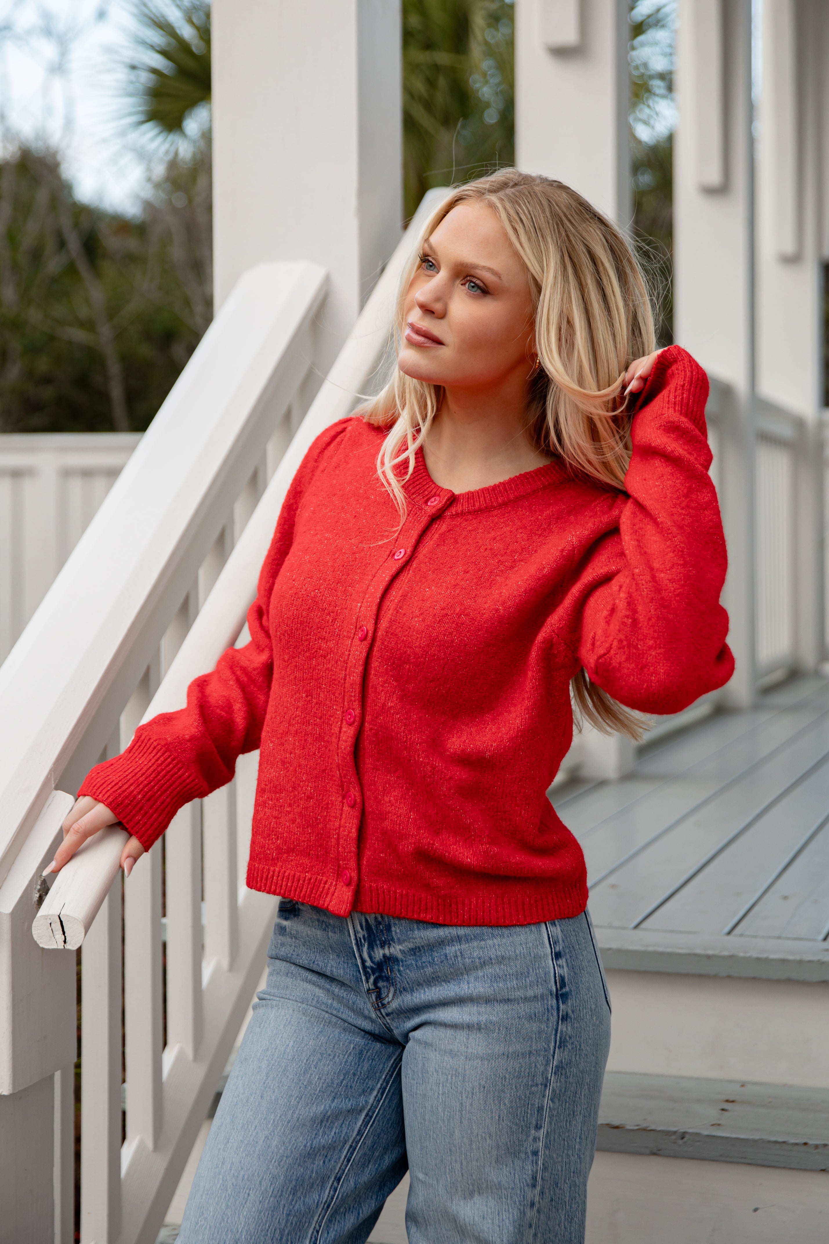 Woman wearing a red sweater and blue jeans standing on a wooden deck.
