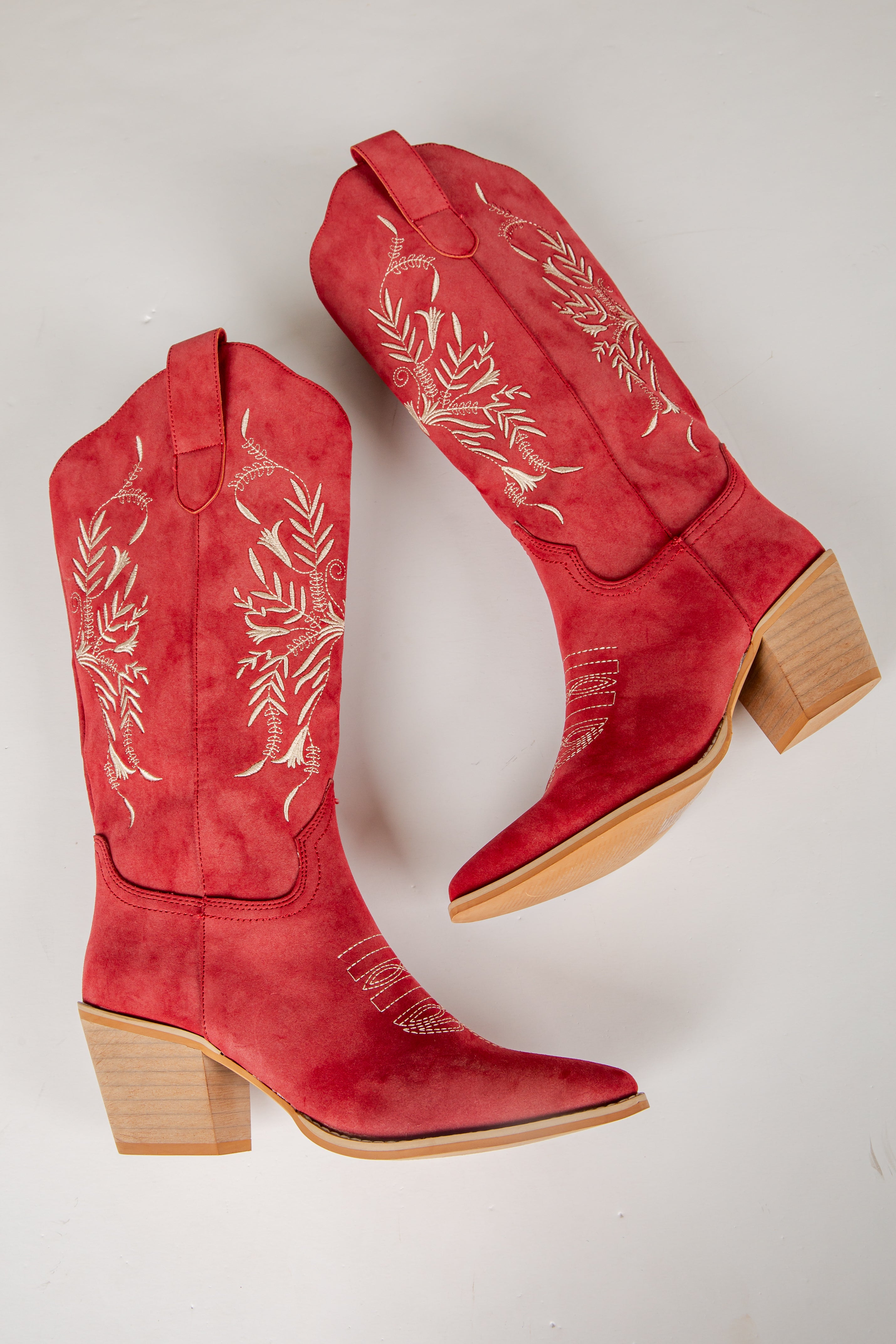 Red cowboy boots with white embroidery on a light gray background