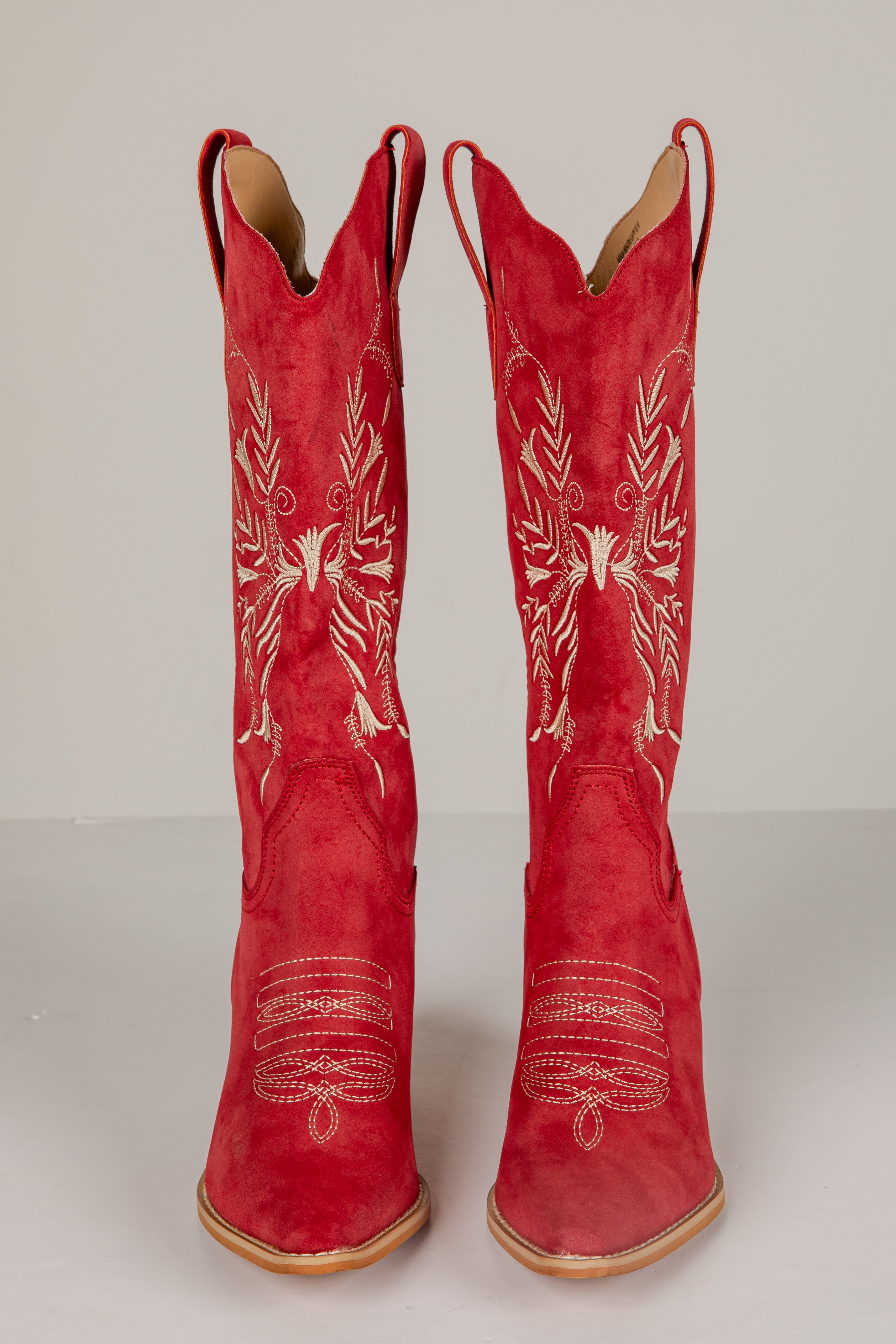 Pair of red cowboy boots with white embroidery on a white background