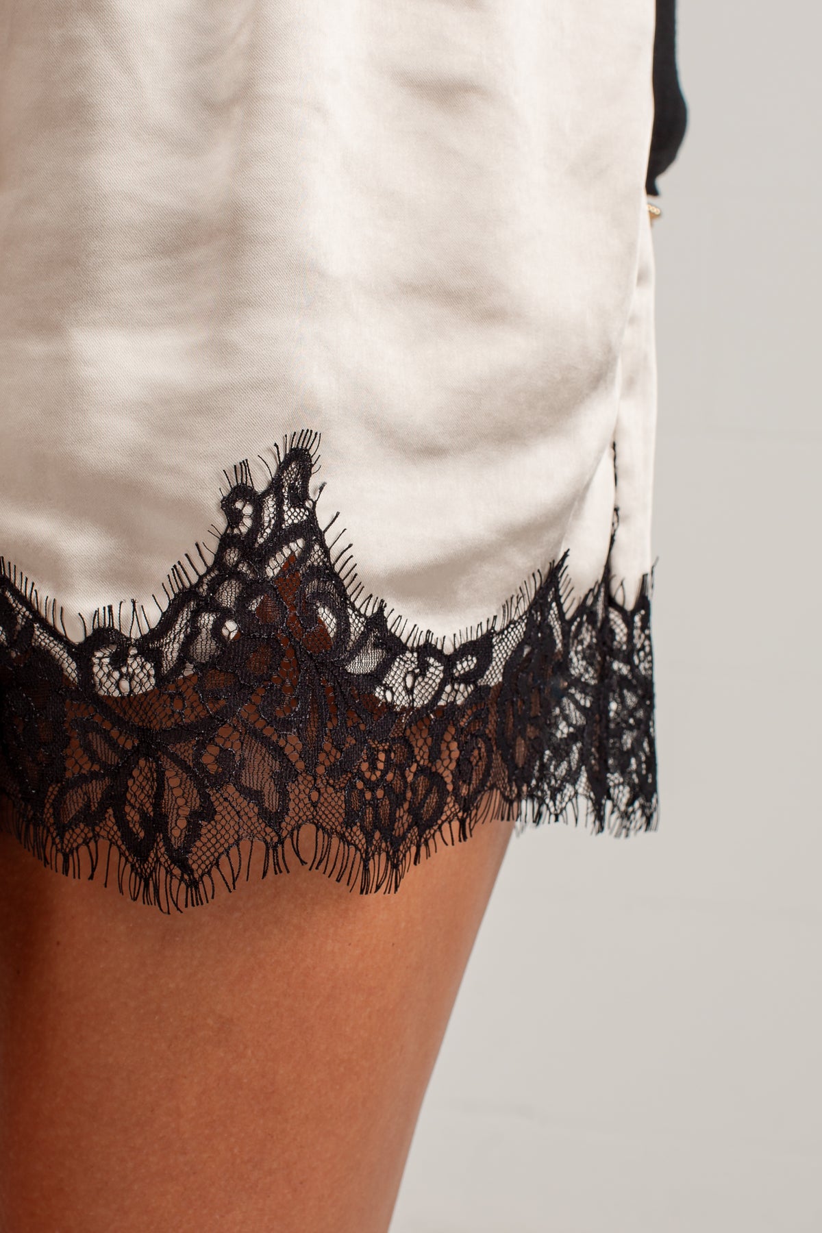 Close-up of a white satin or silk slip dress with a black lace hem, worn by a model.