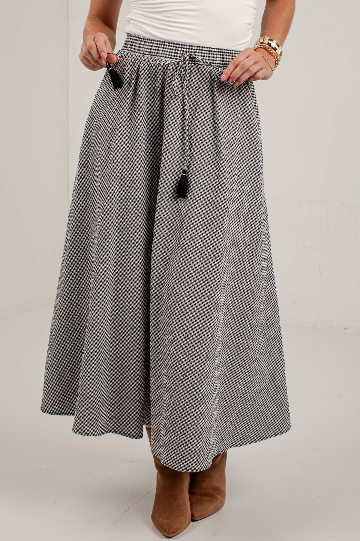 A person wearing a black and white micro-patterned midi skirt with a drawstring waist and black tassels, paired with a white top and brown ankle boots.