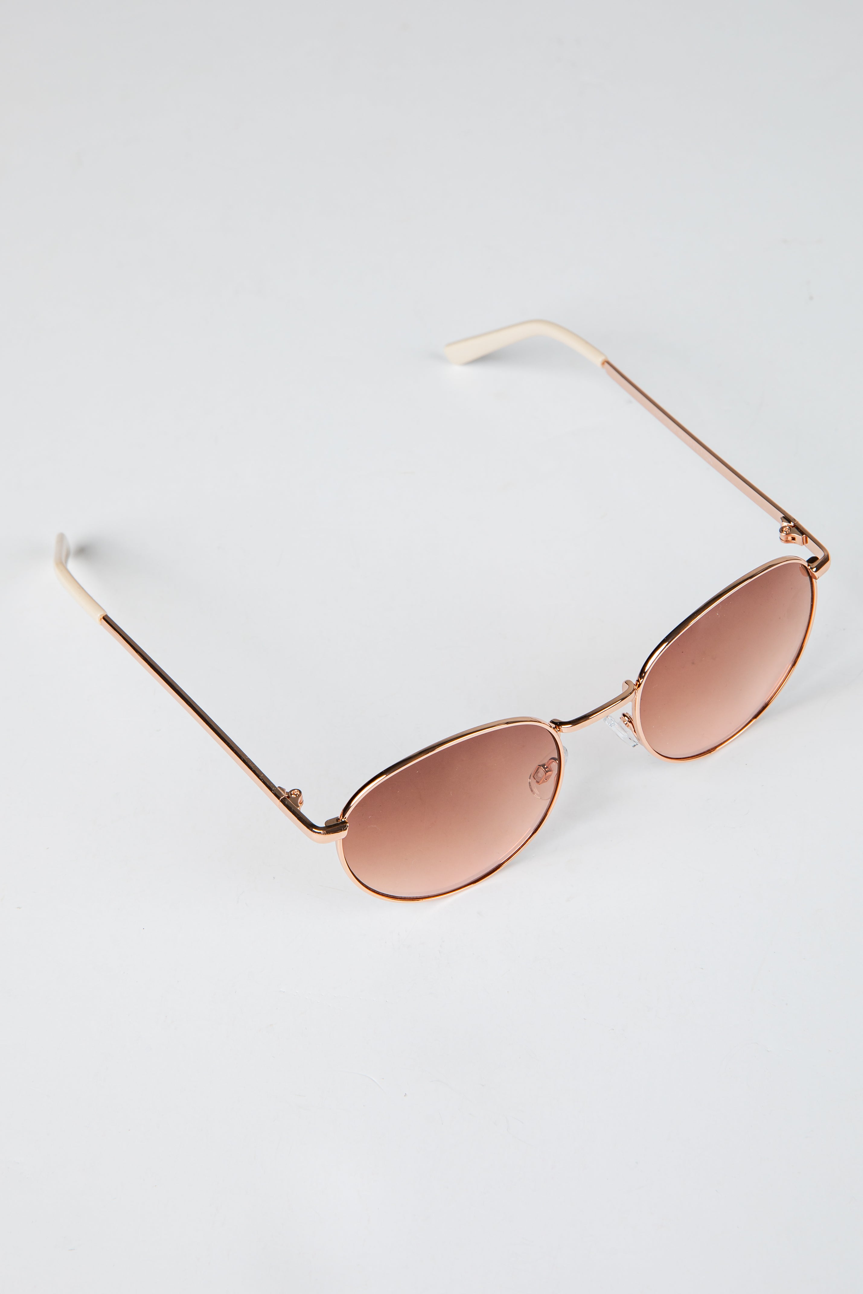 Rose gold sunglasses with pink lenses on a light gray background