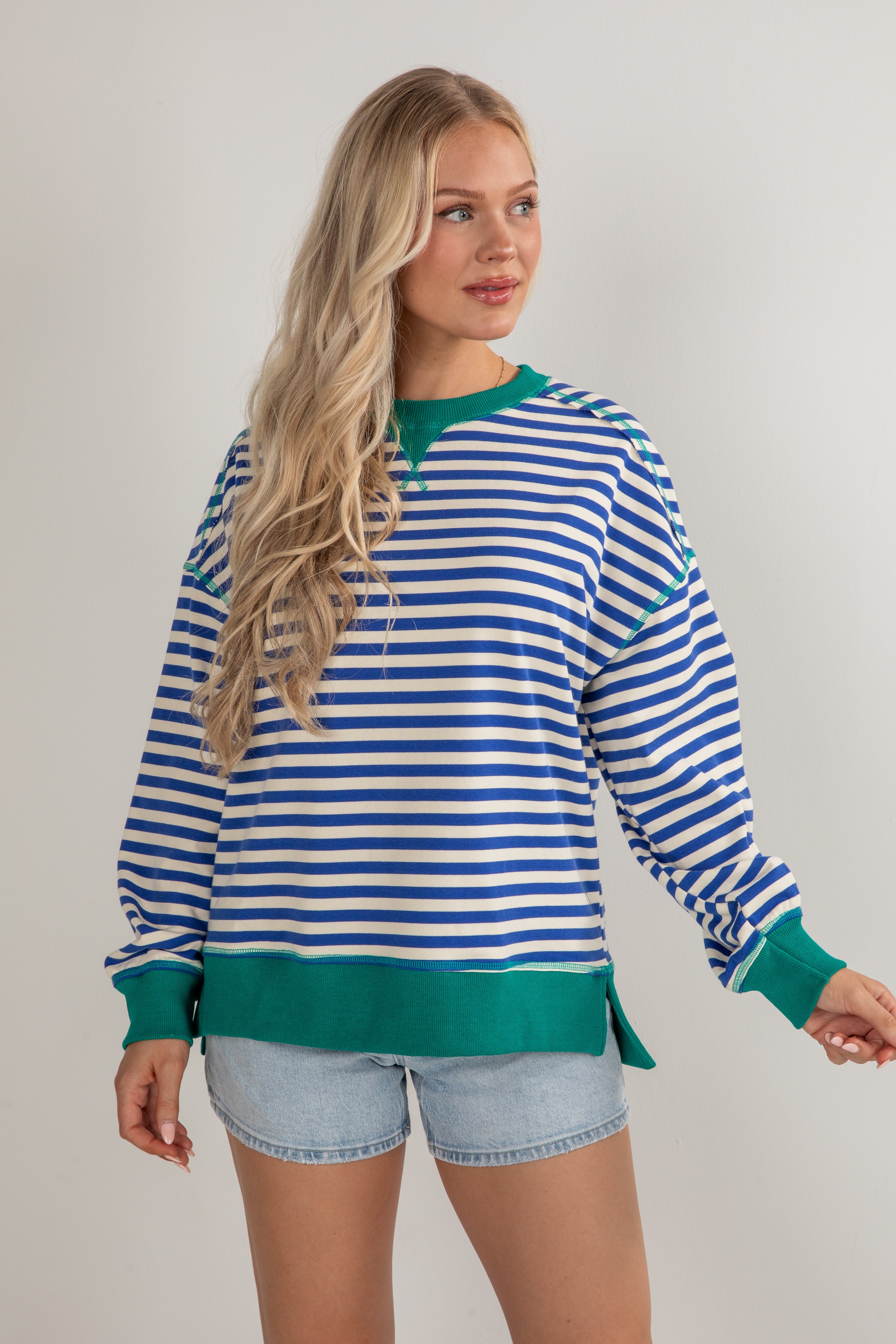 Woman wearing a blue and white striped sweater with green trim on a plain background