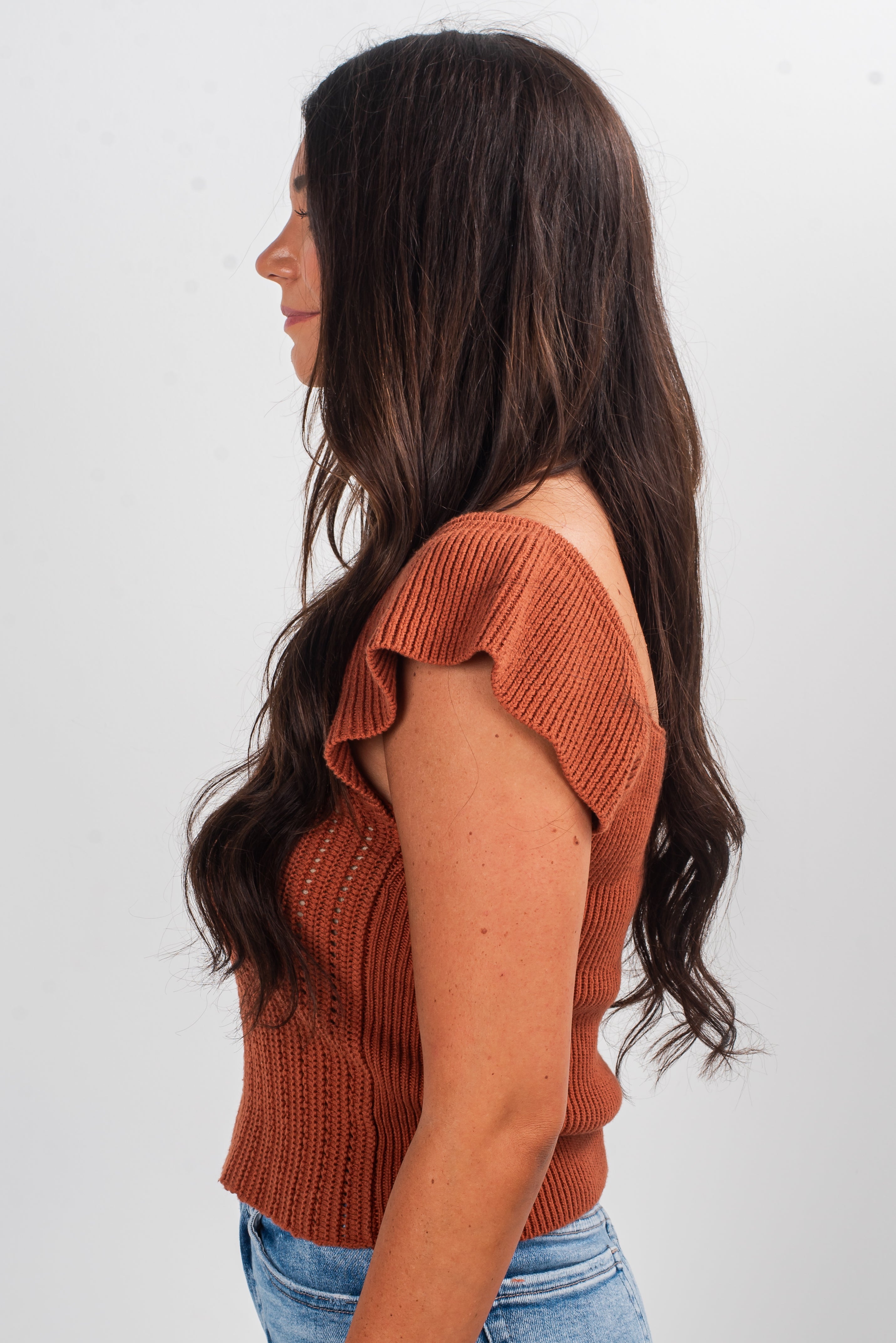 Woman wearing a rust-colored knit top against a white background