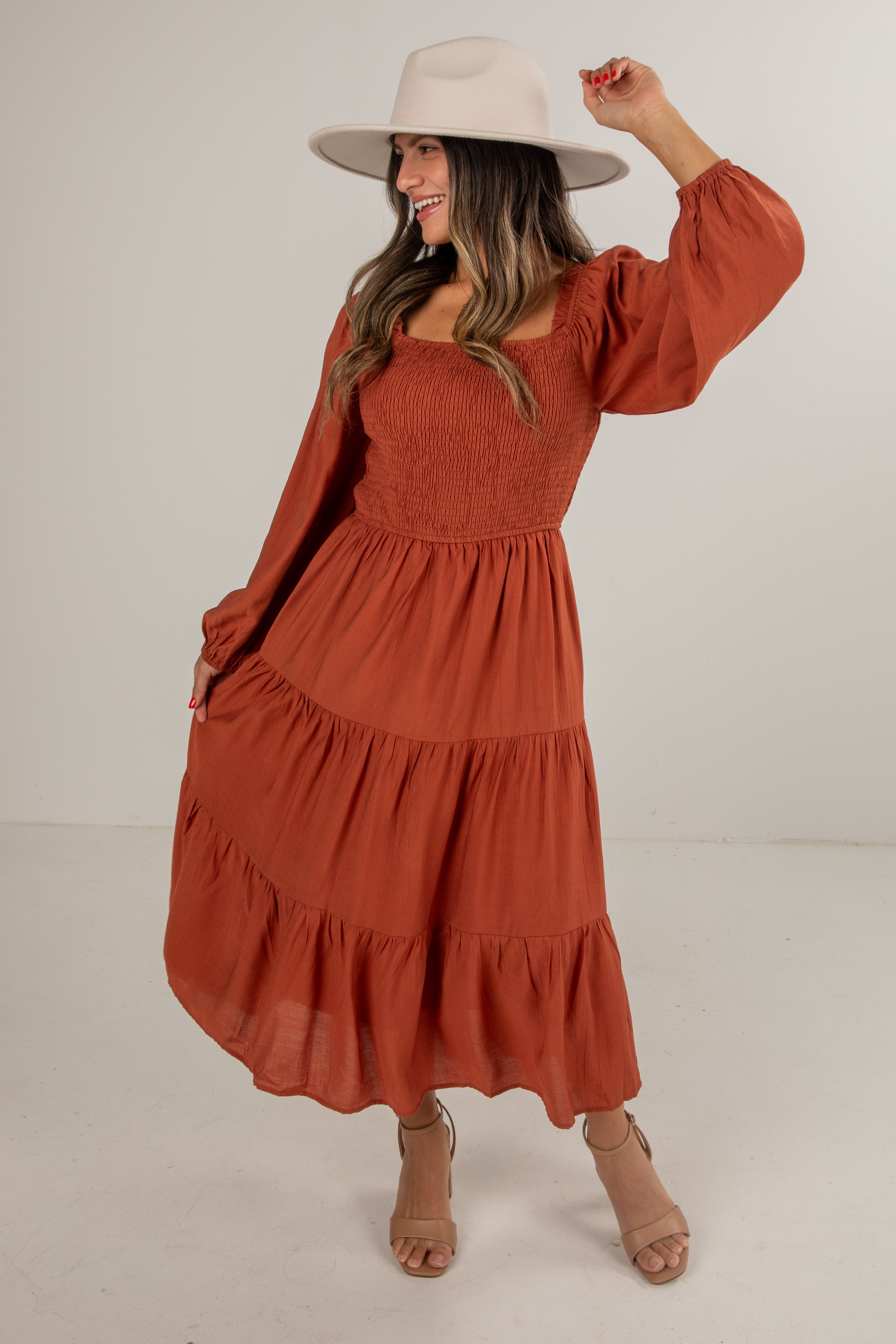 Woman wearing a rust-colored dress and beige hat on a white background