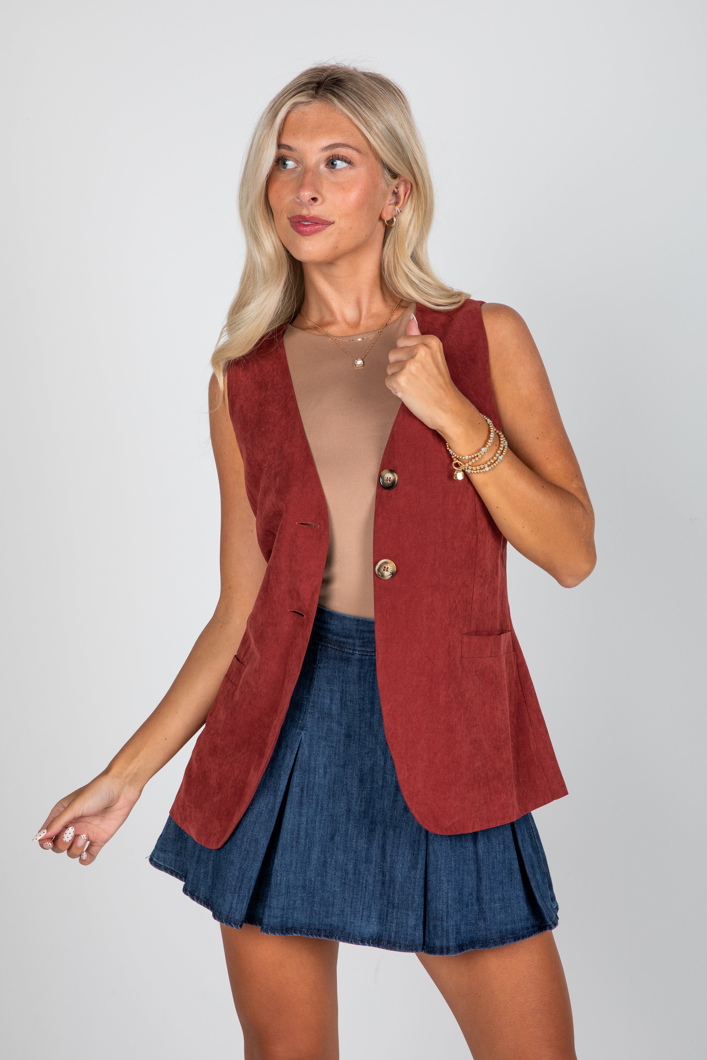 Woman wearing a red vest over a beige top and blue skirt on a white background