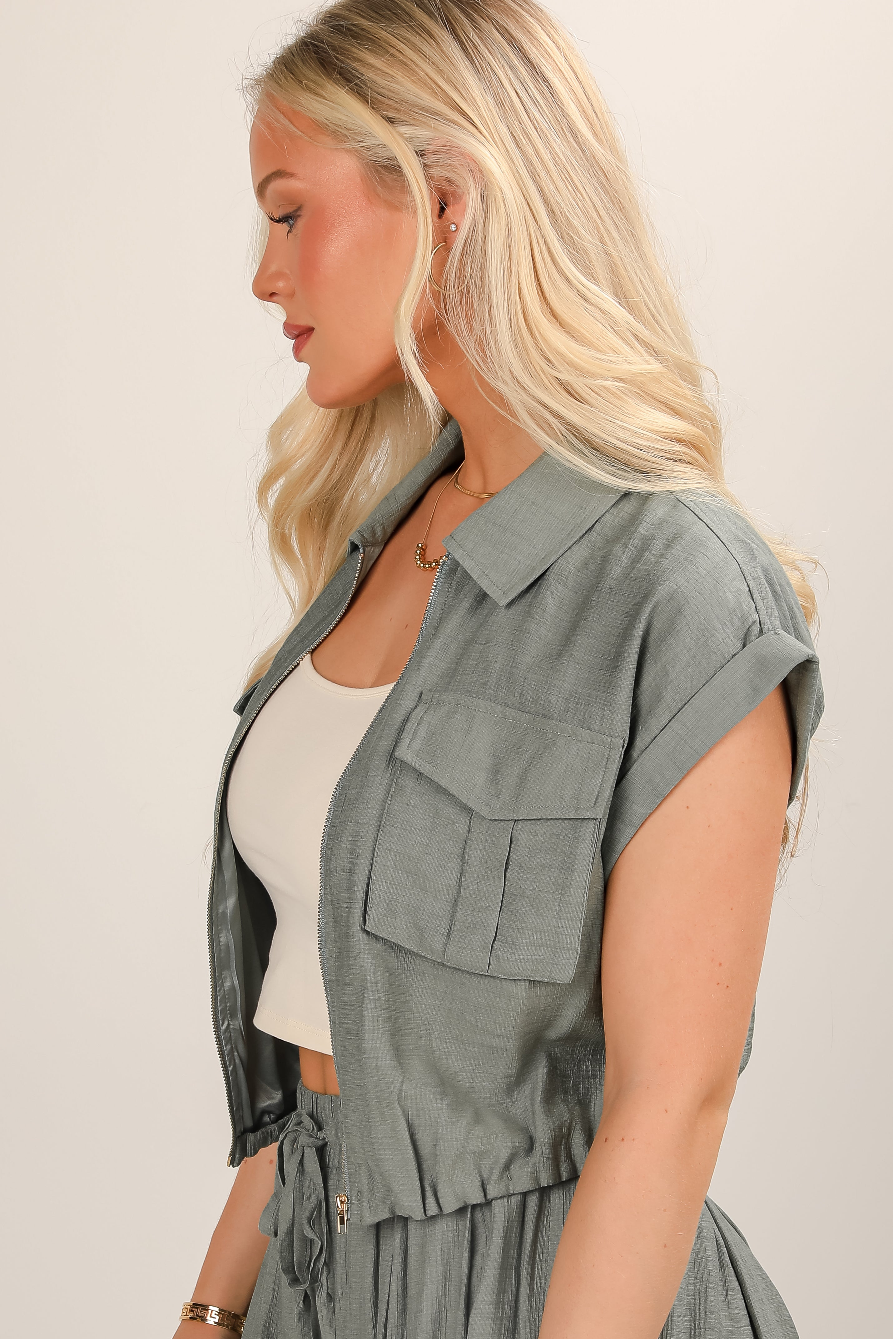 Woman wearing a light gray vest over a white top against a plain background
