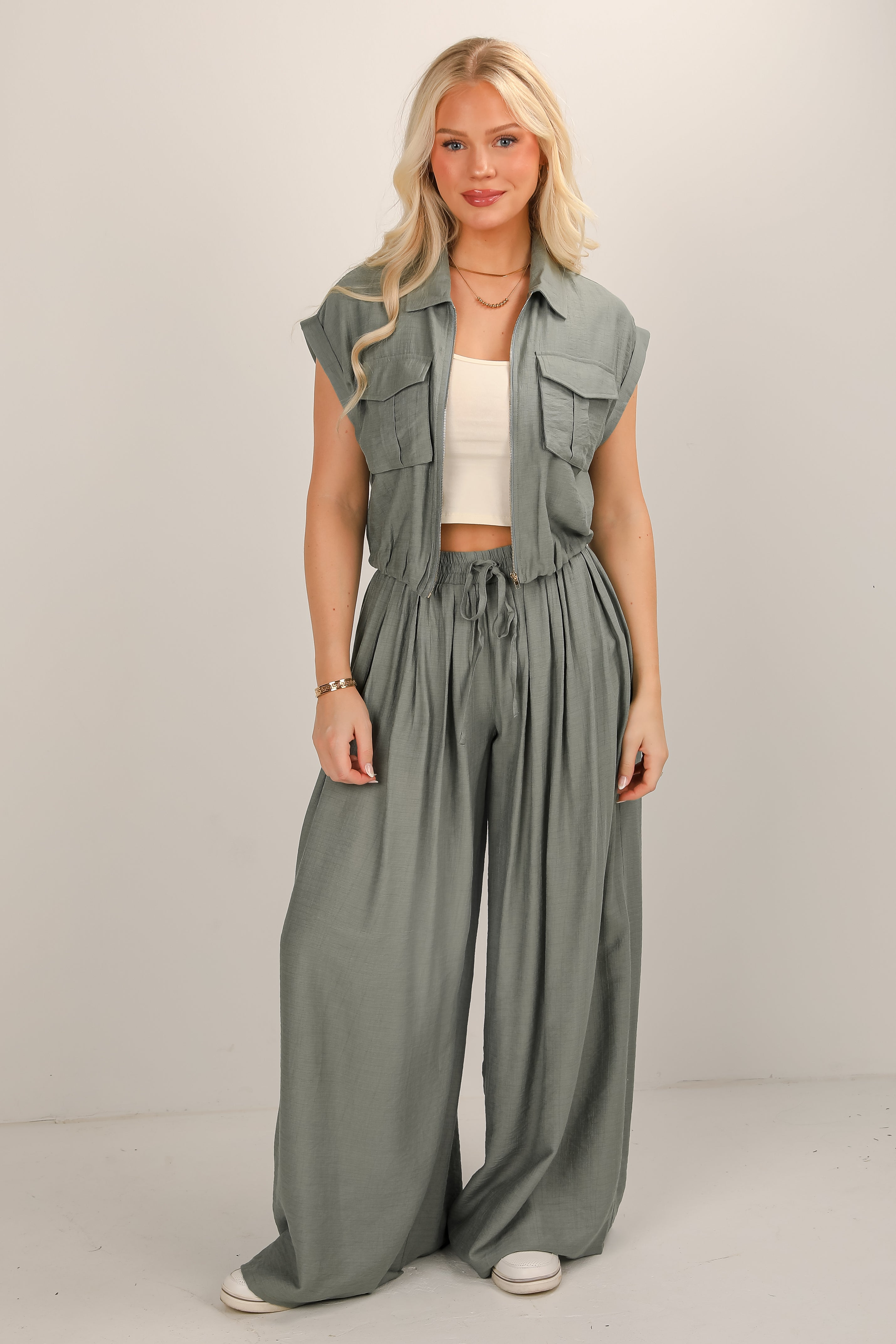 Woman wearing a green sleeveless vest and wide-leg pants on a plain background