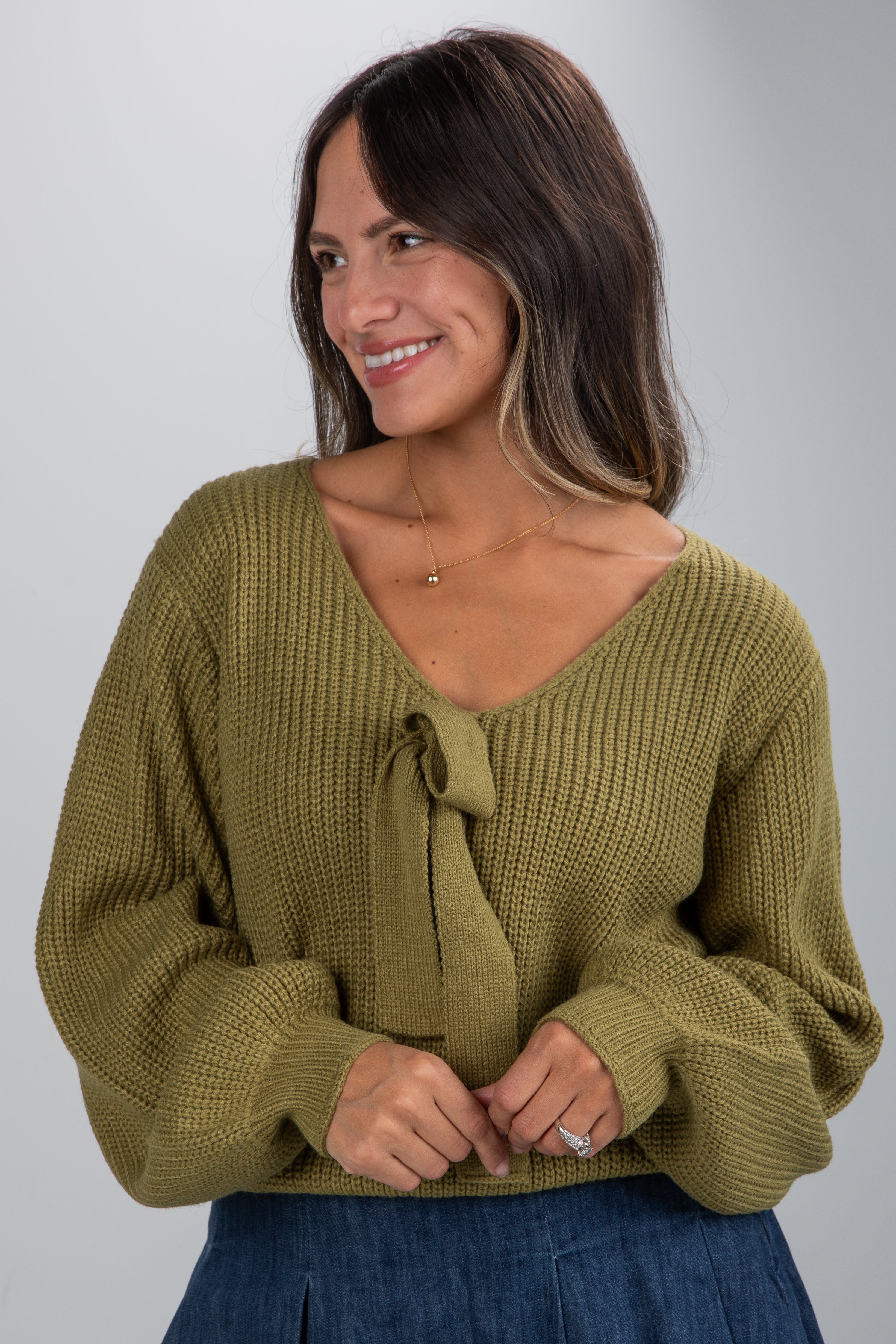 Woman wearing a green knitted sweater with a tie detail on a gray background