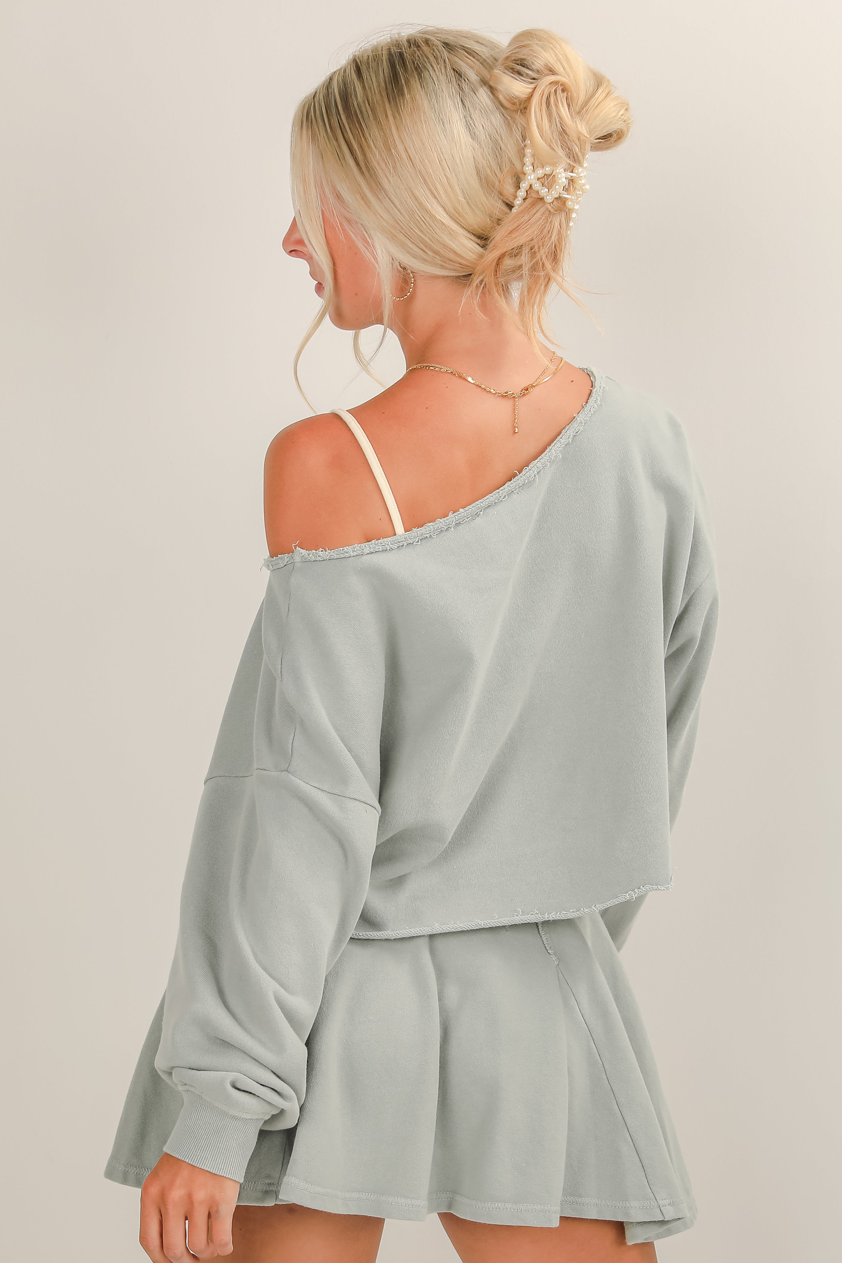 Woman wearing a light gray off-shoulder top and shorts set on a plain background