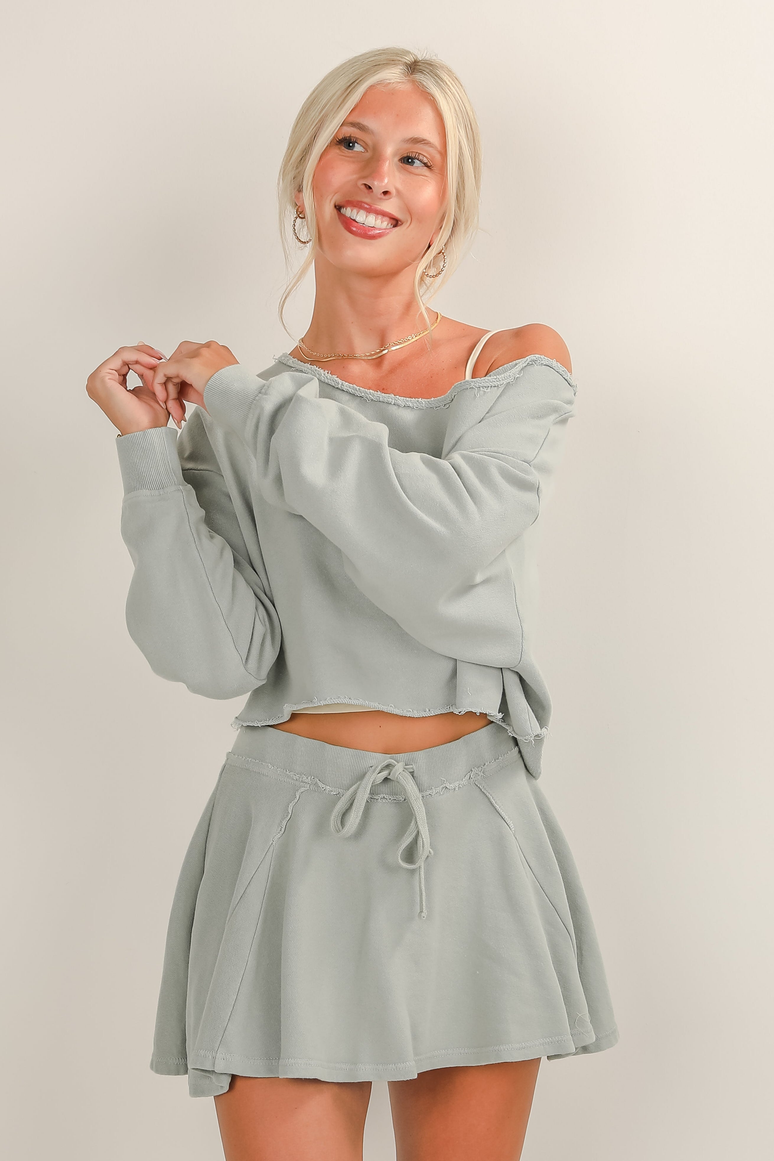 Woman wearing a light gray off-shoulder top and skirt set on a plain background