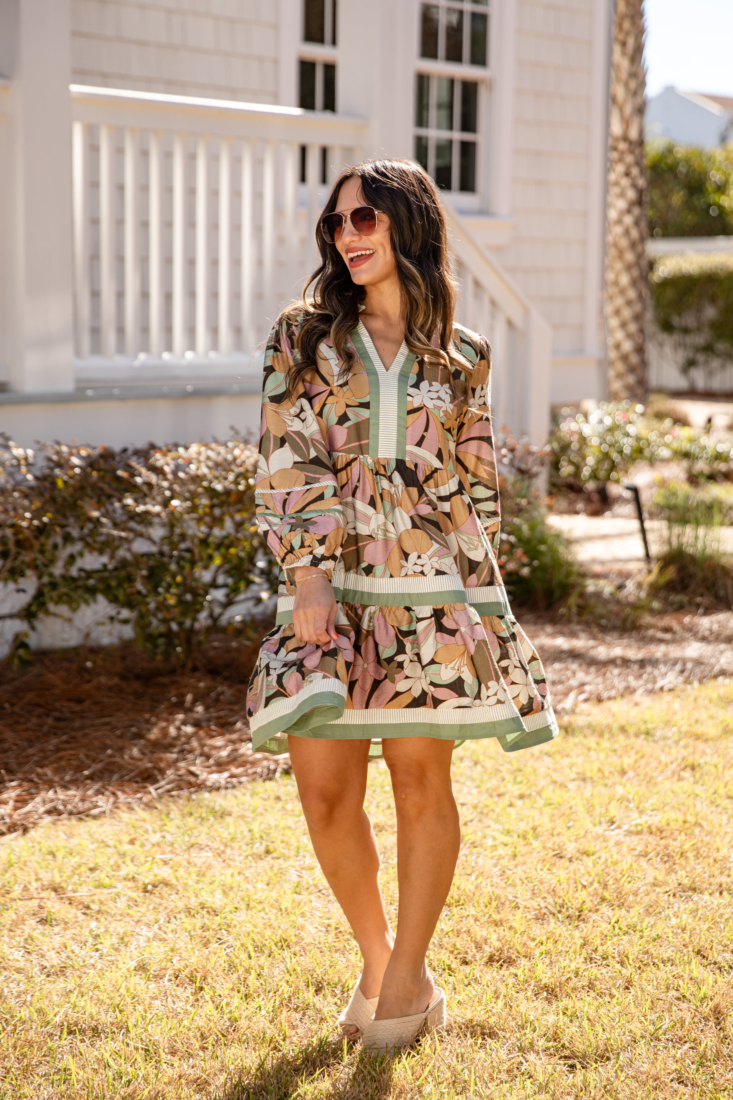 Woman in a patterned dress standing outdoors with a house in the background