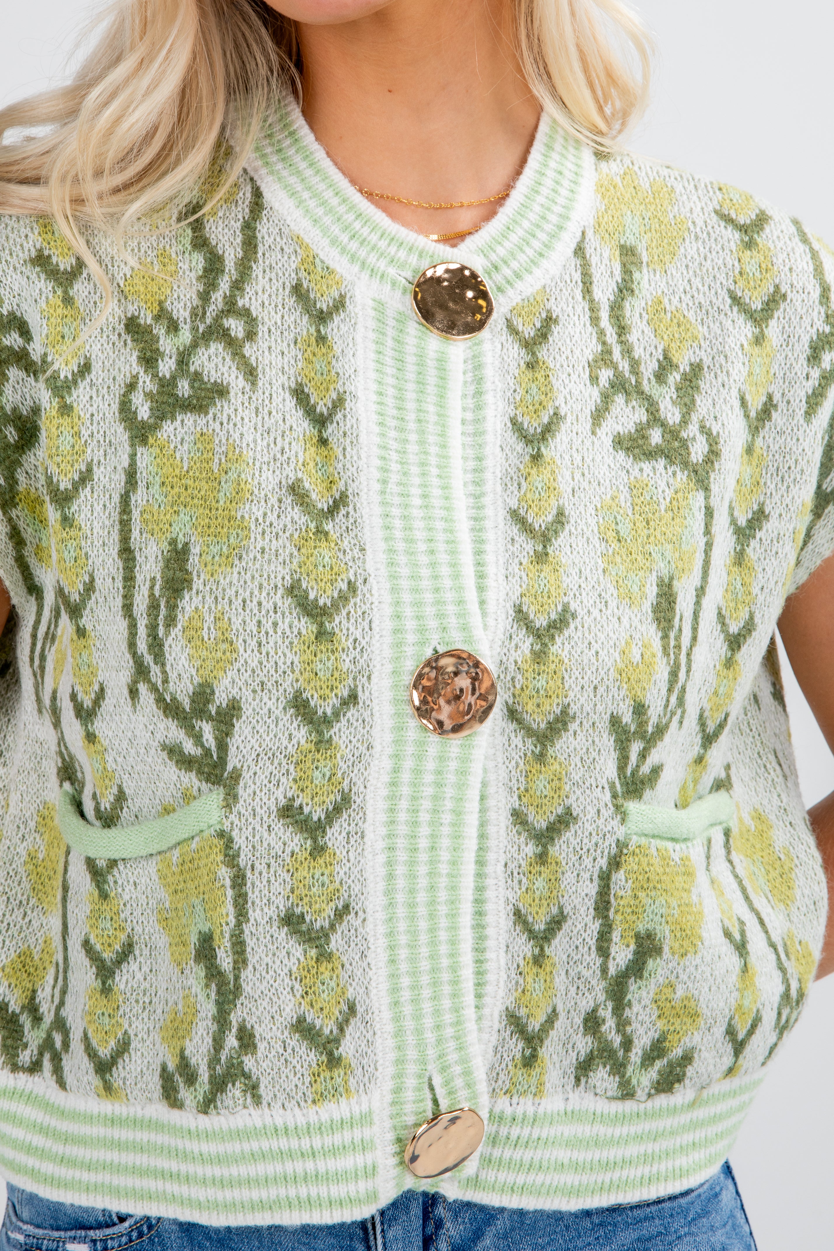 Green knitted cardigan with floral pattern and wooden buttons on a white background