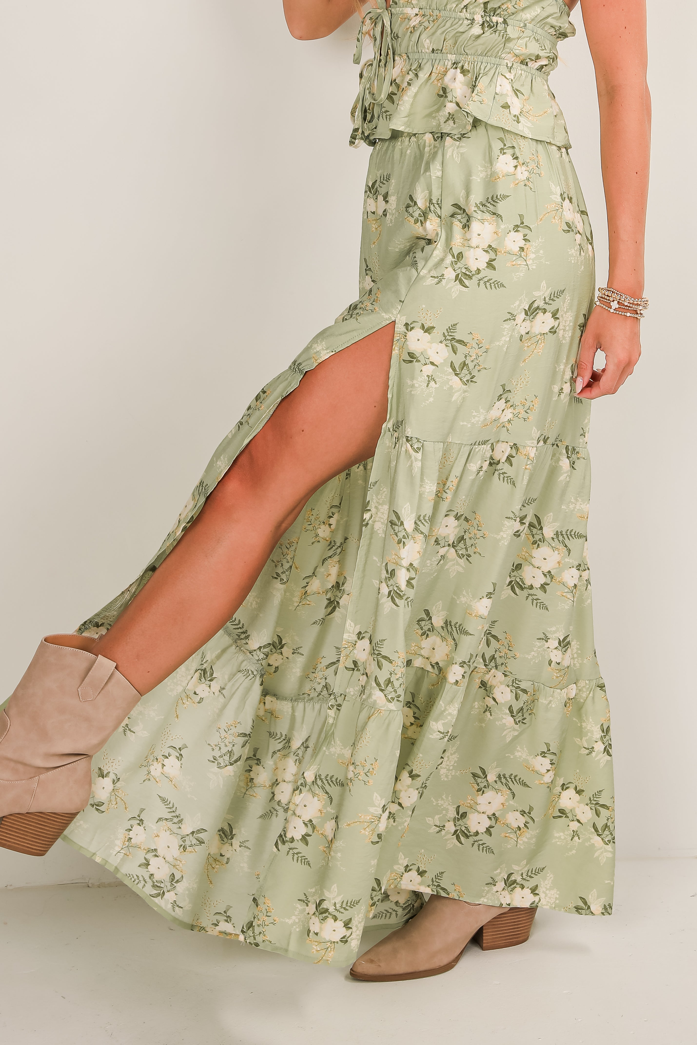 Woman wearing a green floral dress with a slit on a plain background