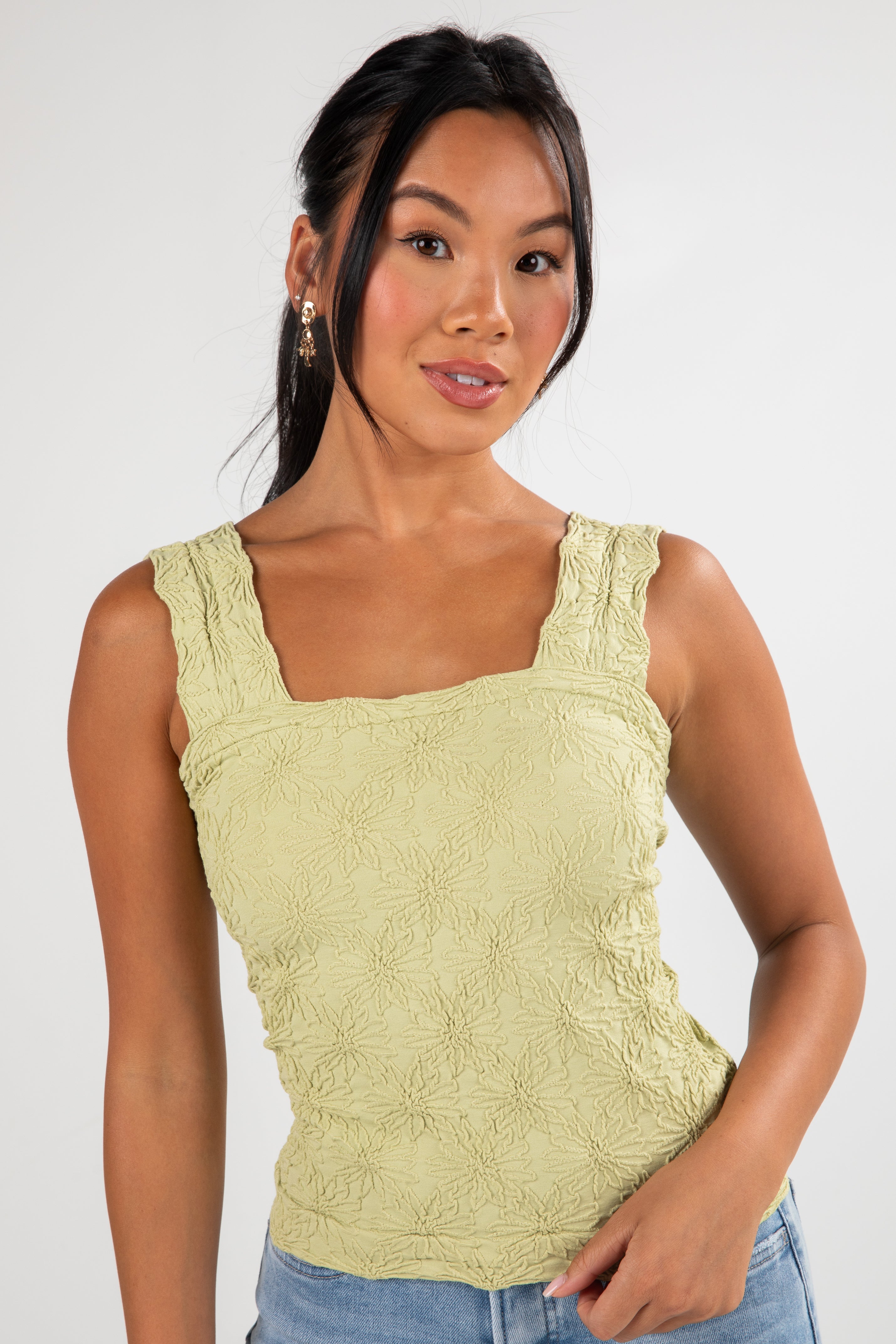 Woman wearing a light green sleeveless top against a white background