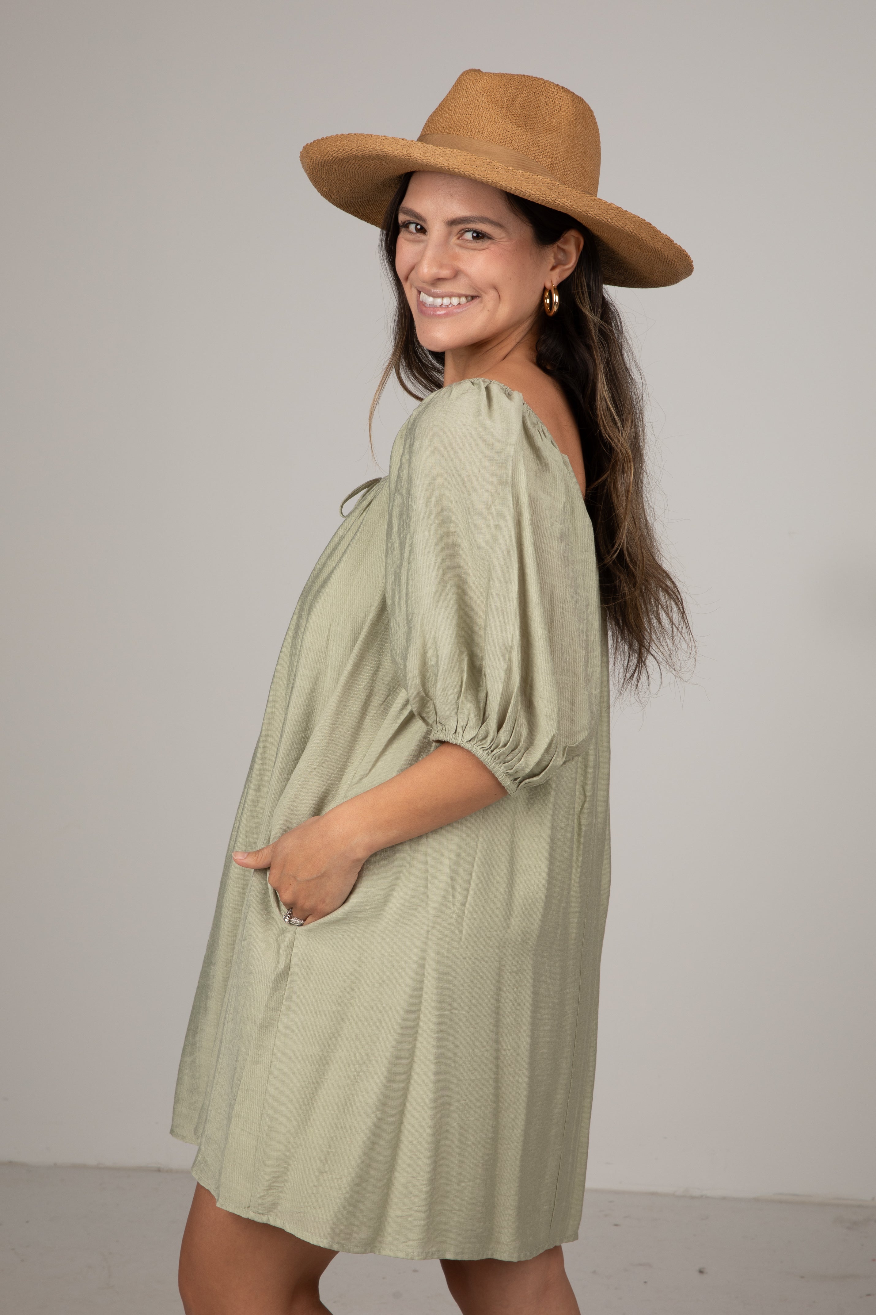 Woman wearing a green dress and brown hat against a plain background