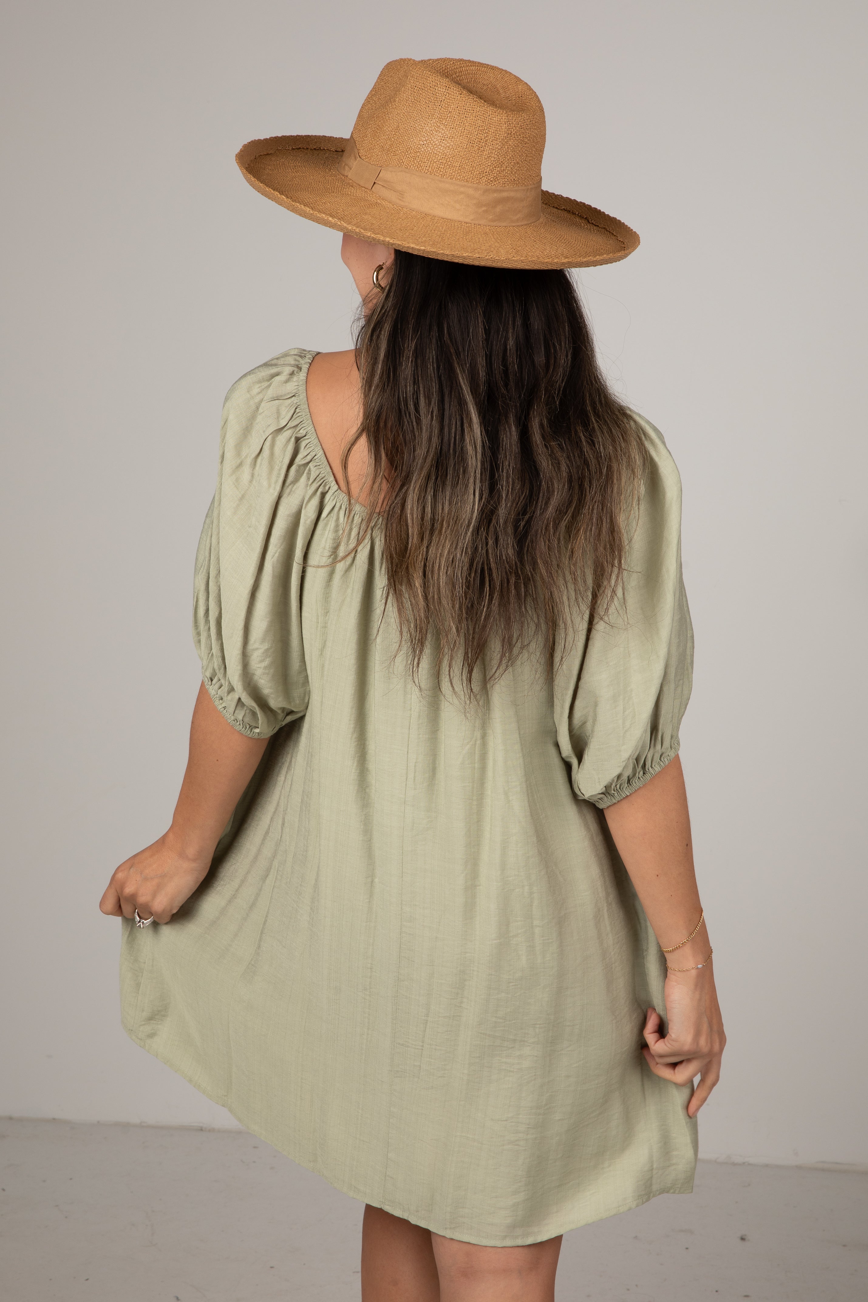 Woman wearing a light green dress and brown hat against a plain background