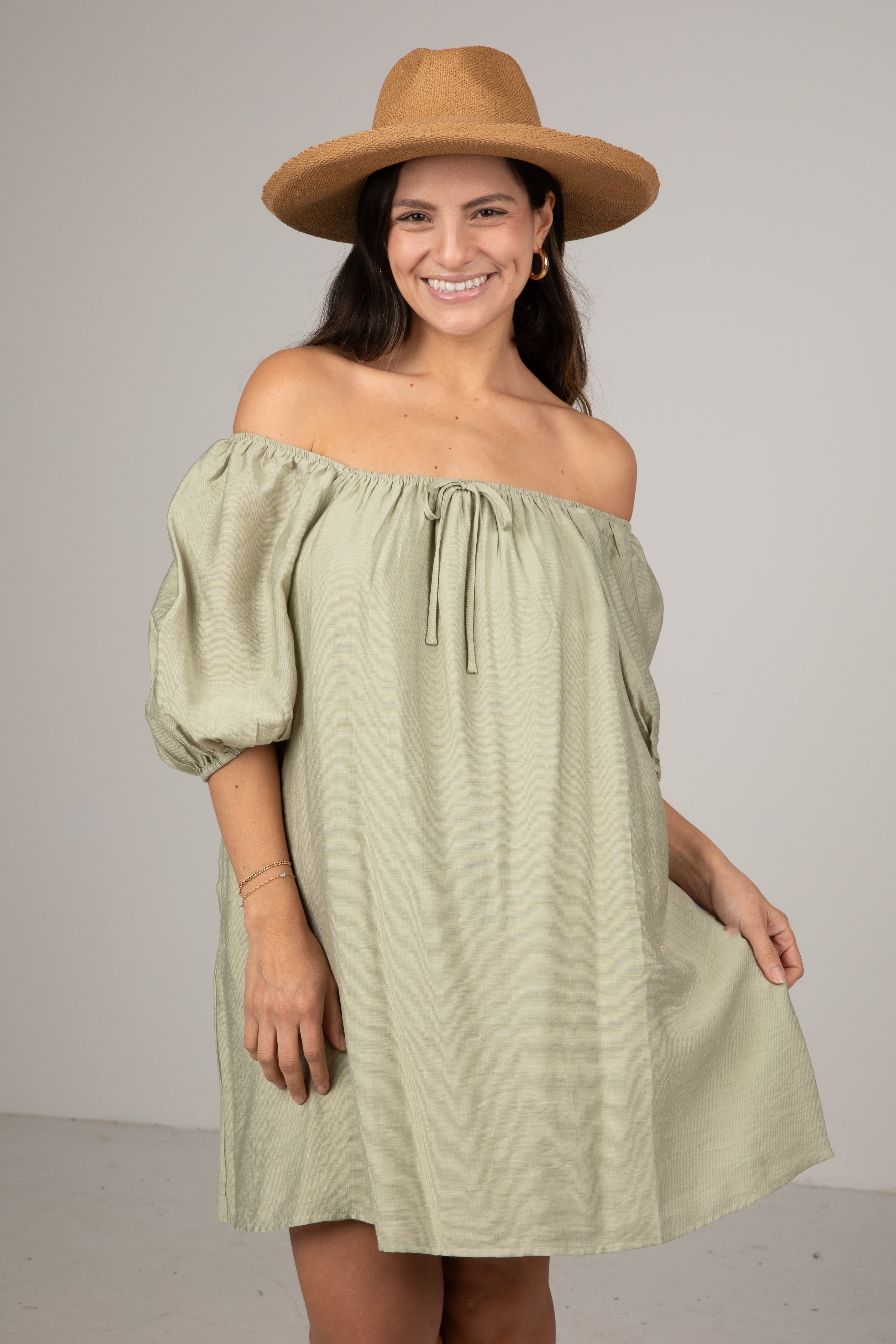 Woman wearing a green off-shoulder dress and brown hat against a plain background