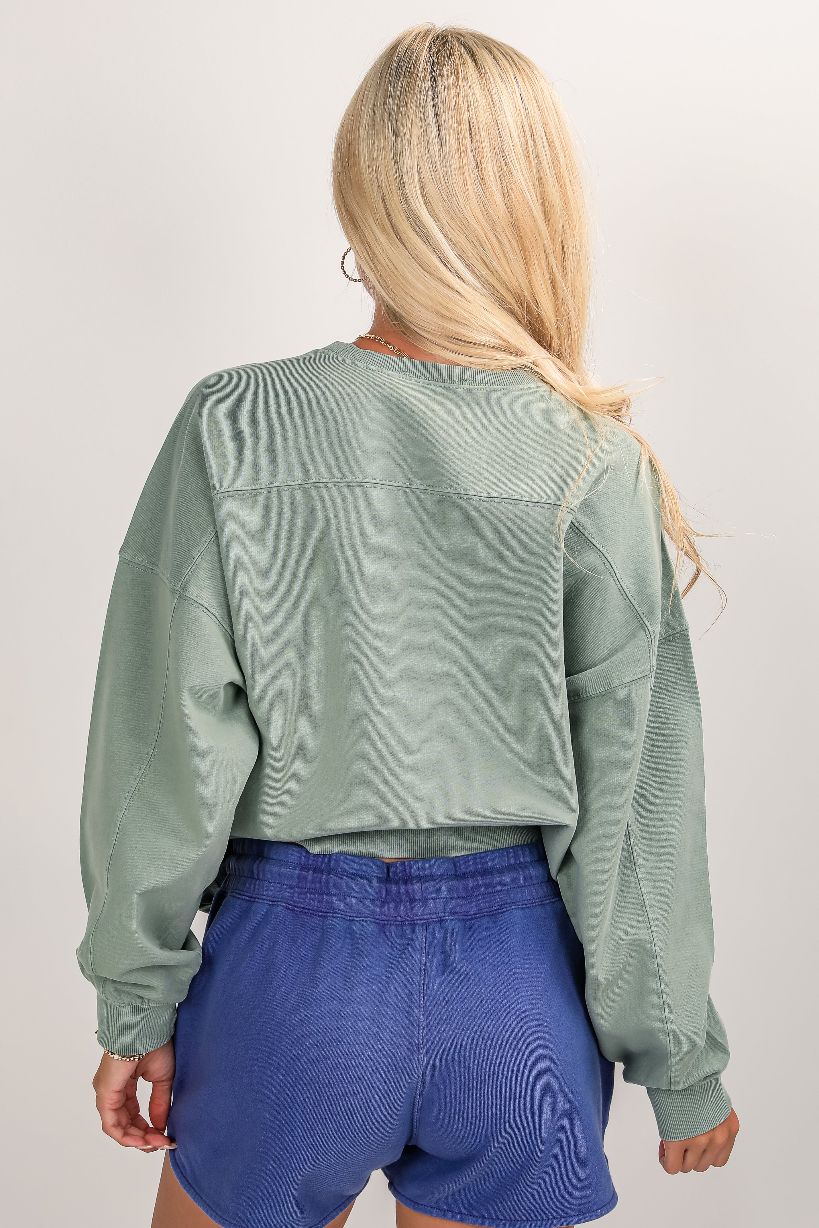 Person wearing a green sweatshirt and blue shorts on a plain background