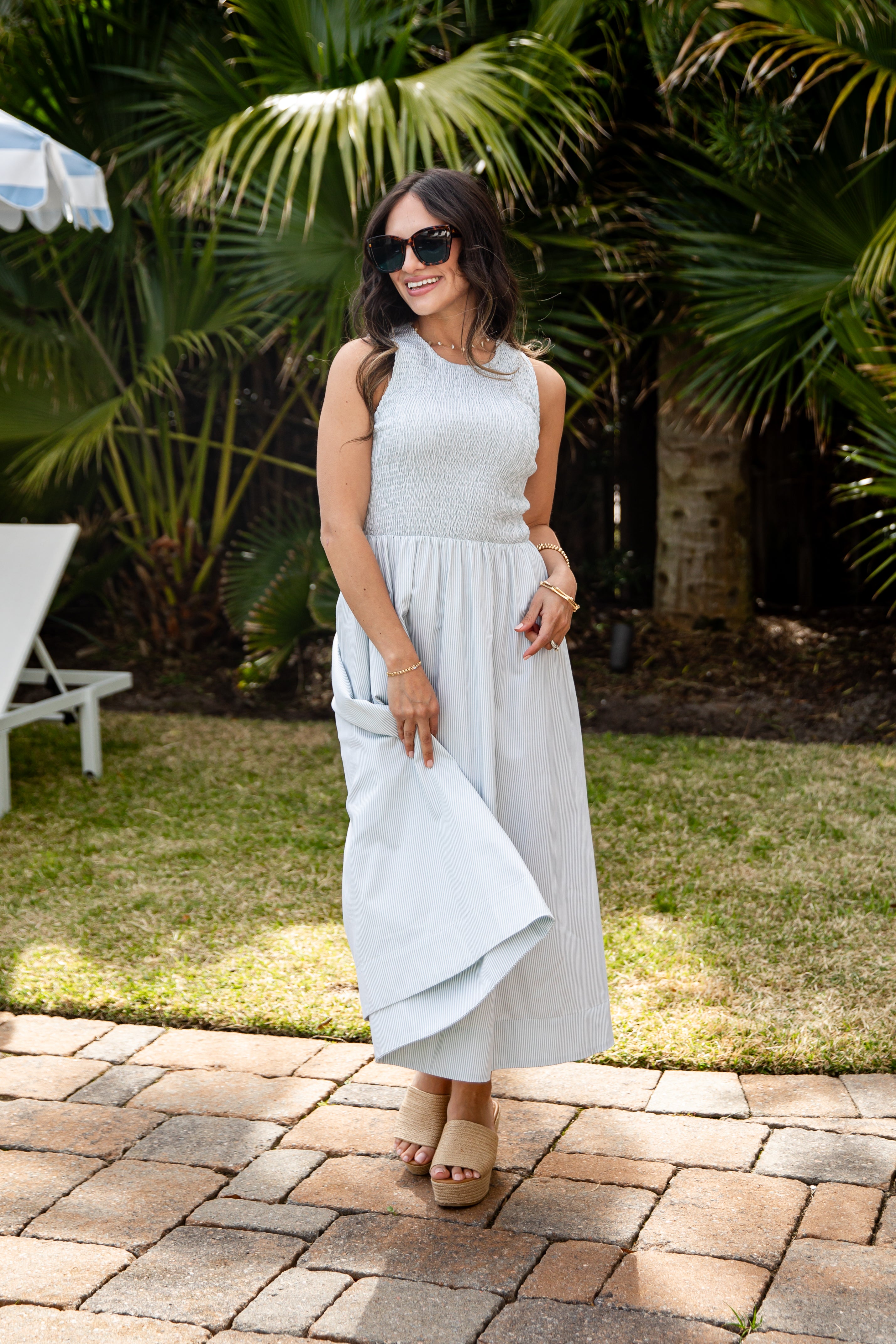 Woman in a light gray dress standing outdoors with greenery in the background
