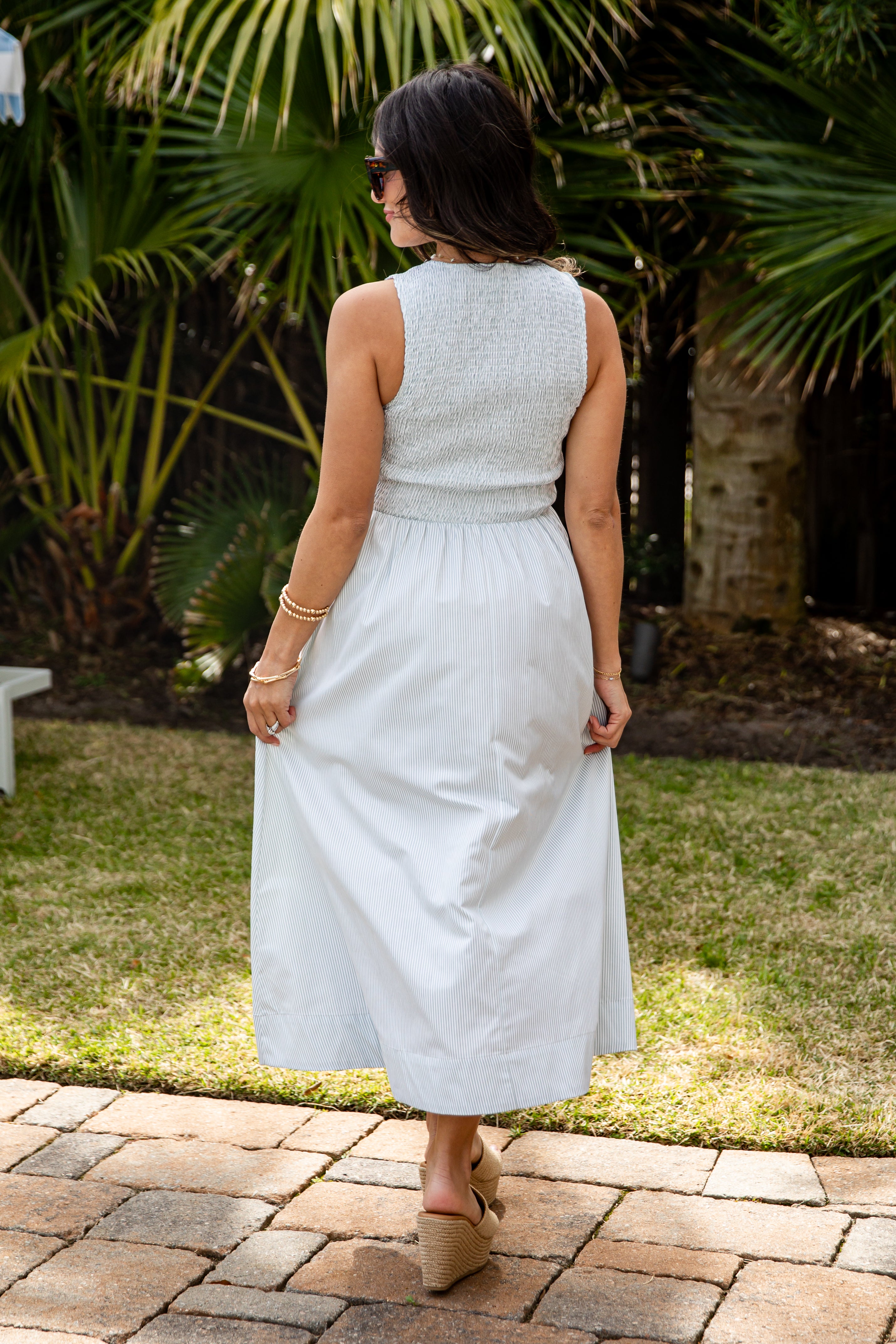 Woman in a light gray dress standing outdoors with greenery in the background