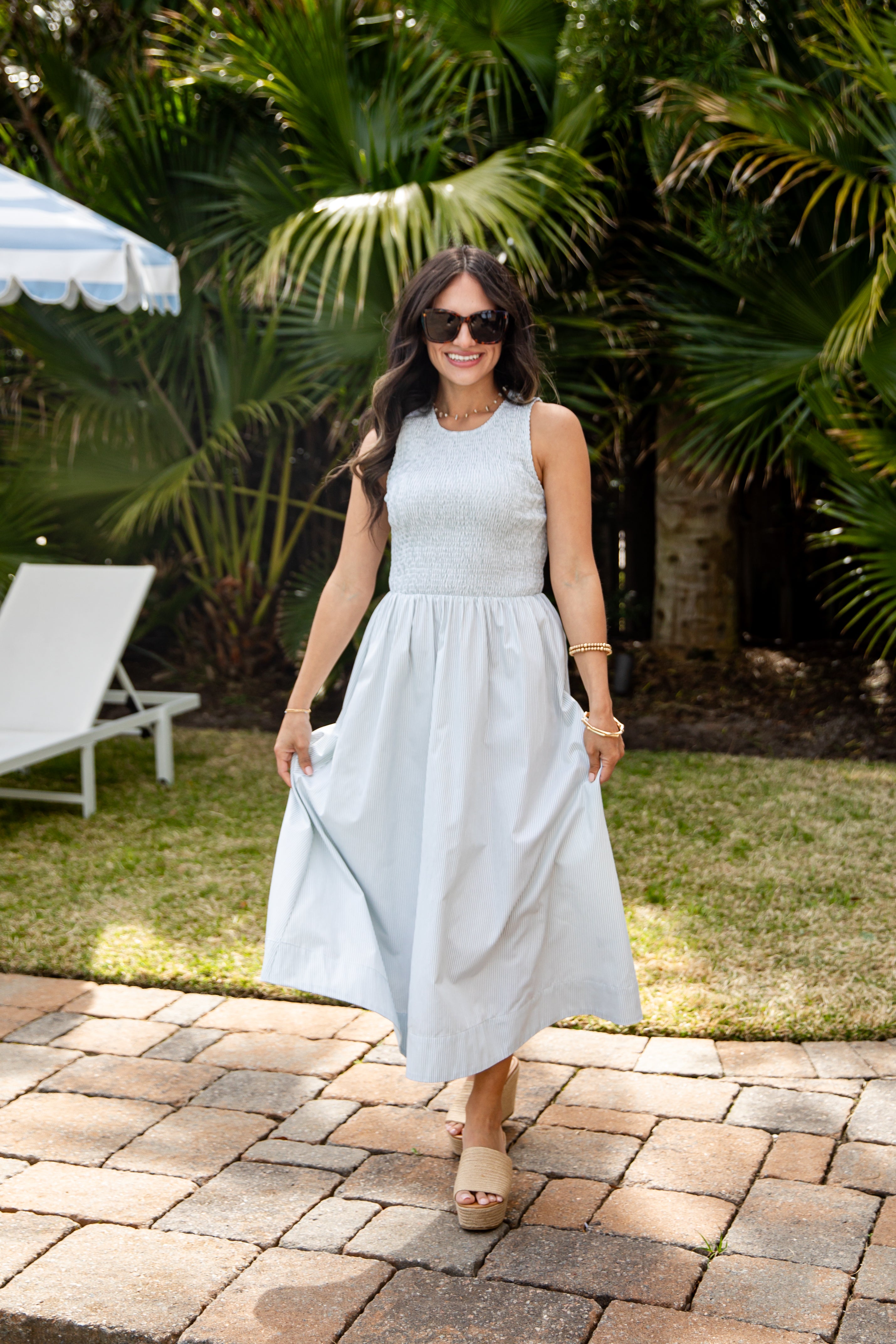 Woman in a light blue dress standing outdoors with greenery in the background