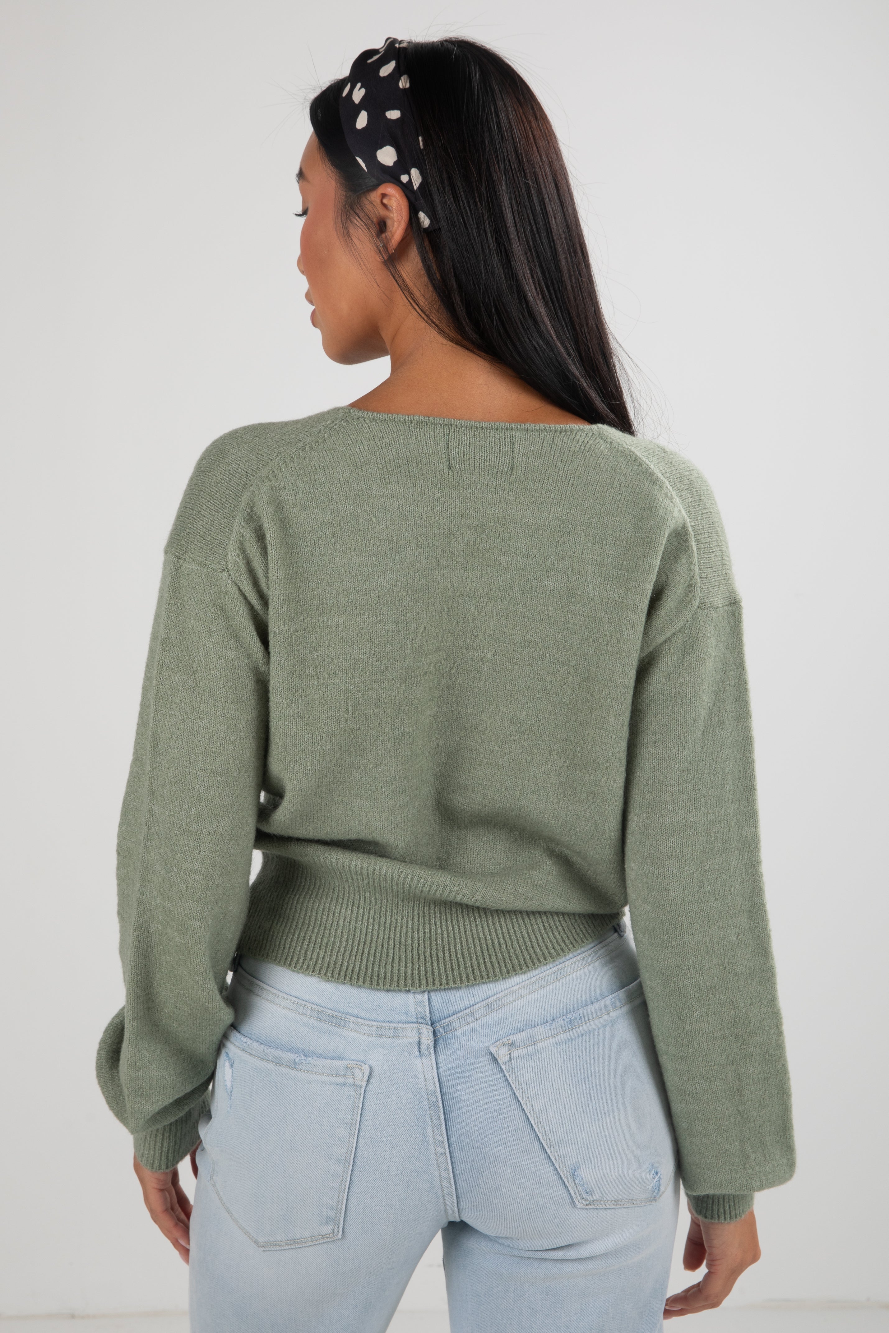 Person wearing a green sweater and light blue jeans with a white background