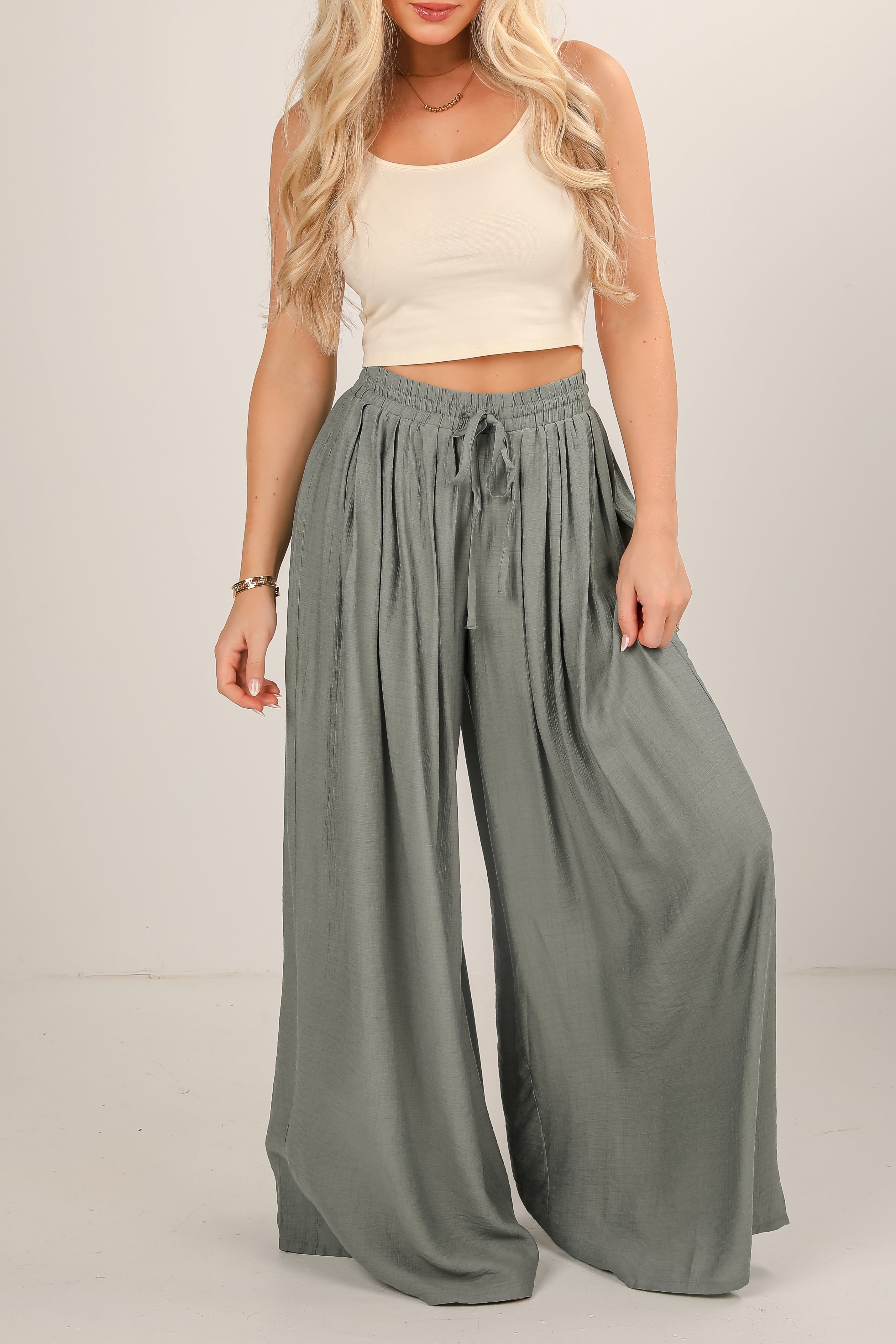 Woman wearing a beige top and gray wide-leg pants on a plain background