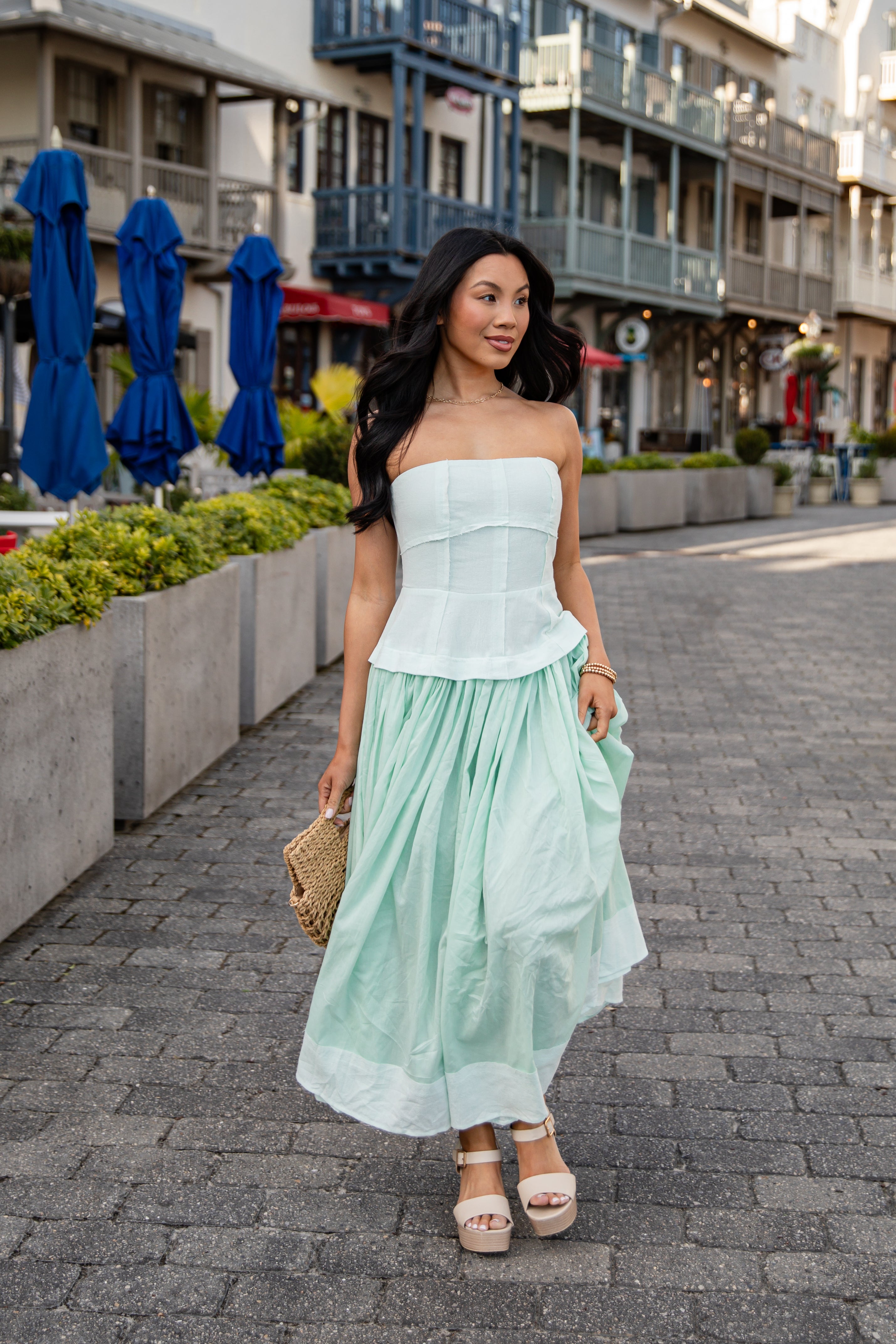 Woman in a light green strapless top and skirt standing on a city street.