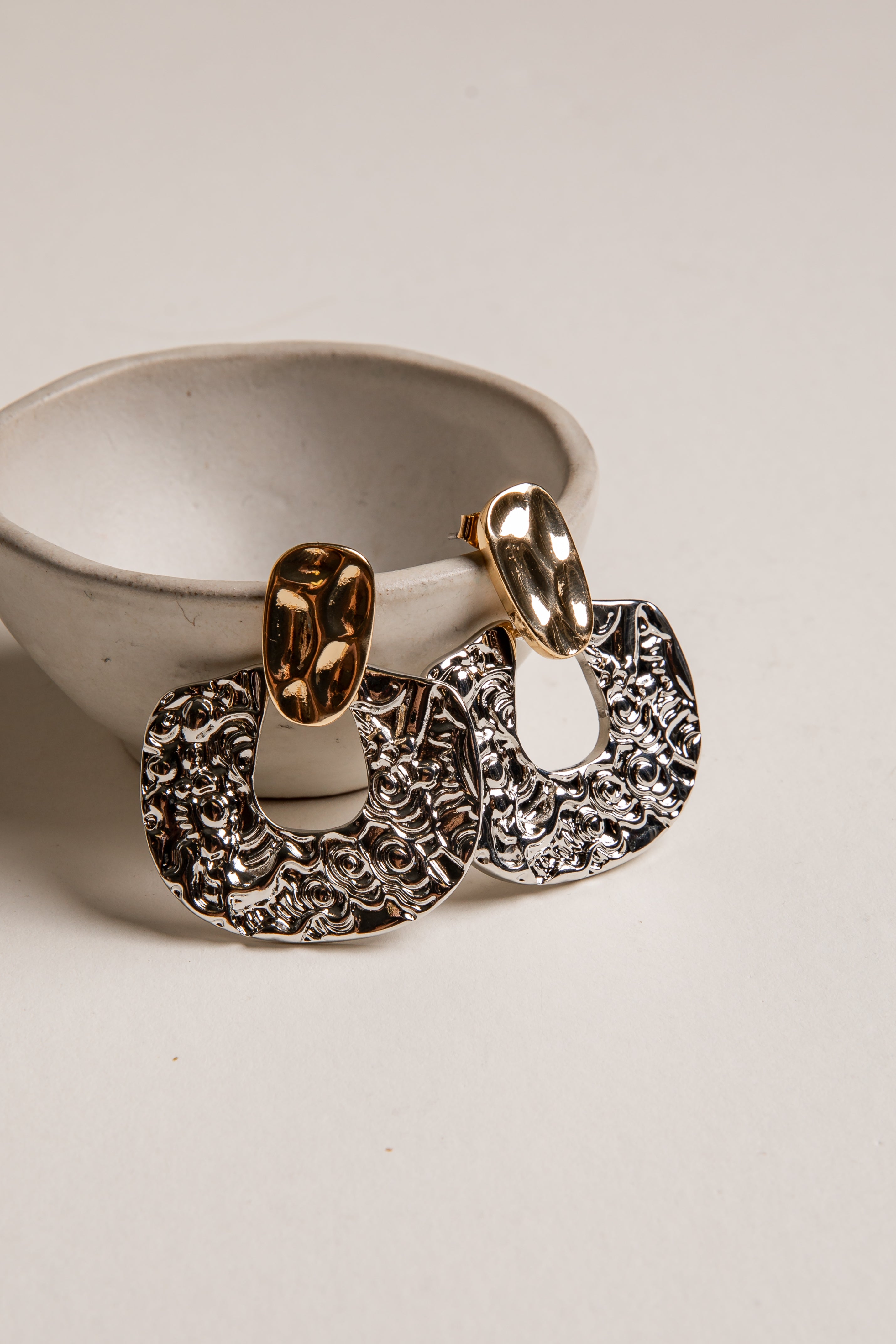 Gold and silver hoop earrings on a white surface with a neutral background