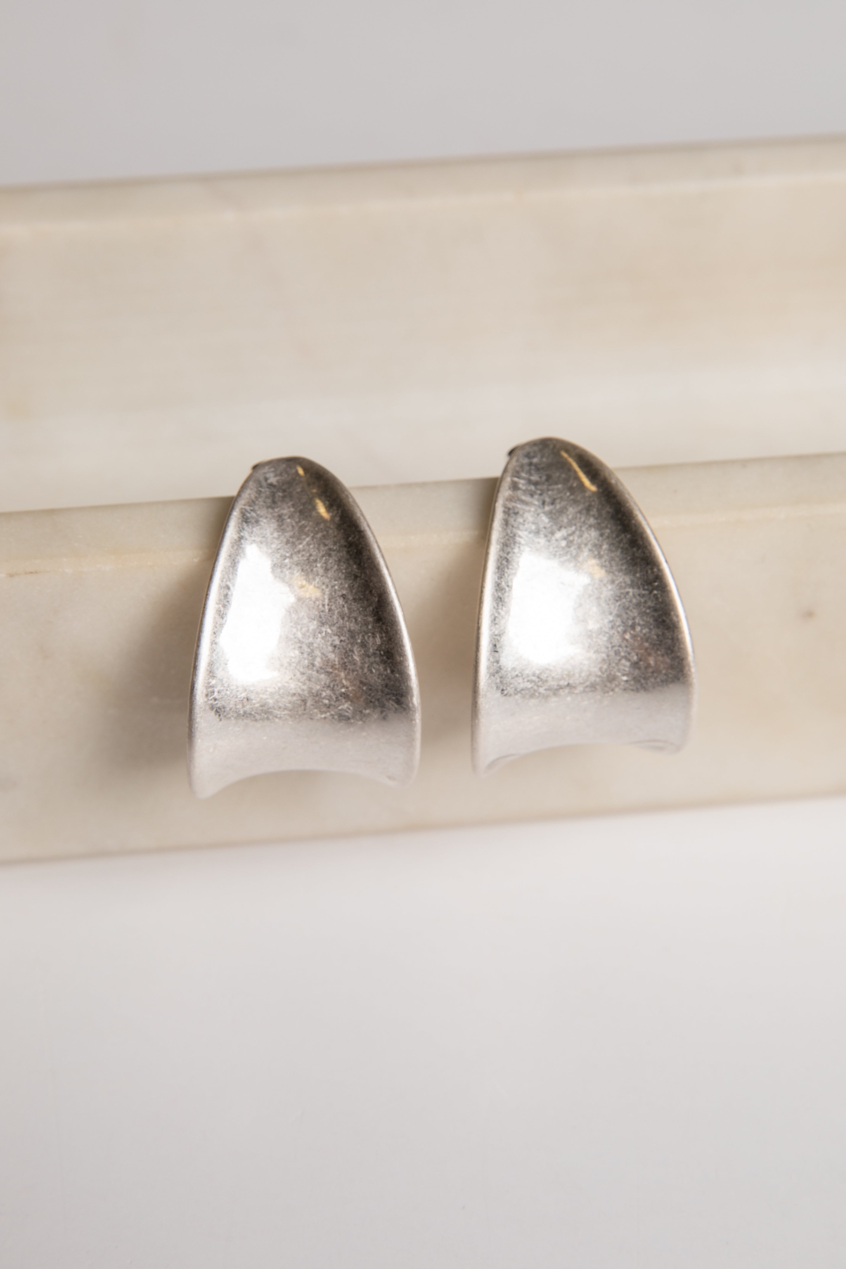 Pair of silver earrings on a light wooden stick against a white background