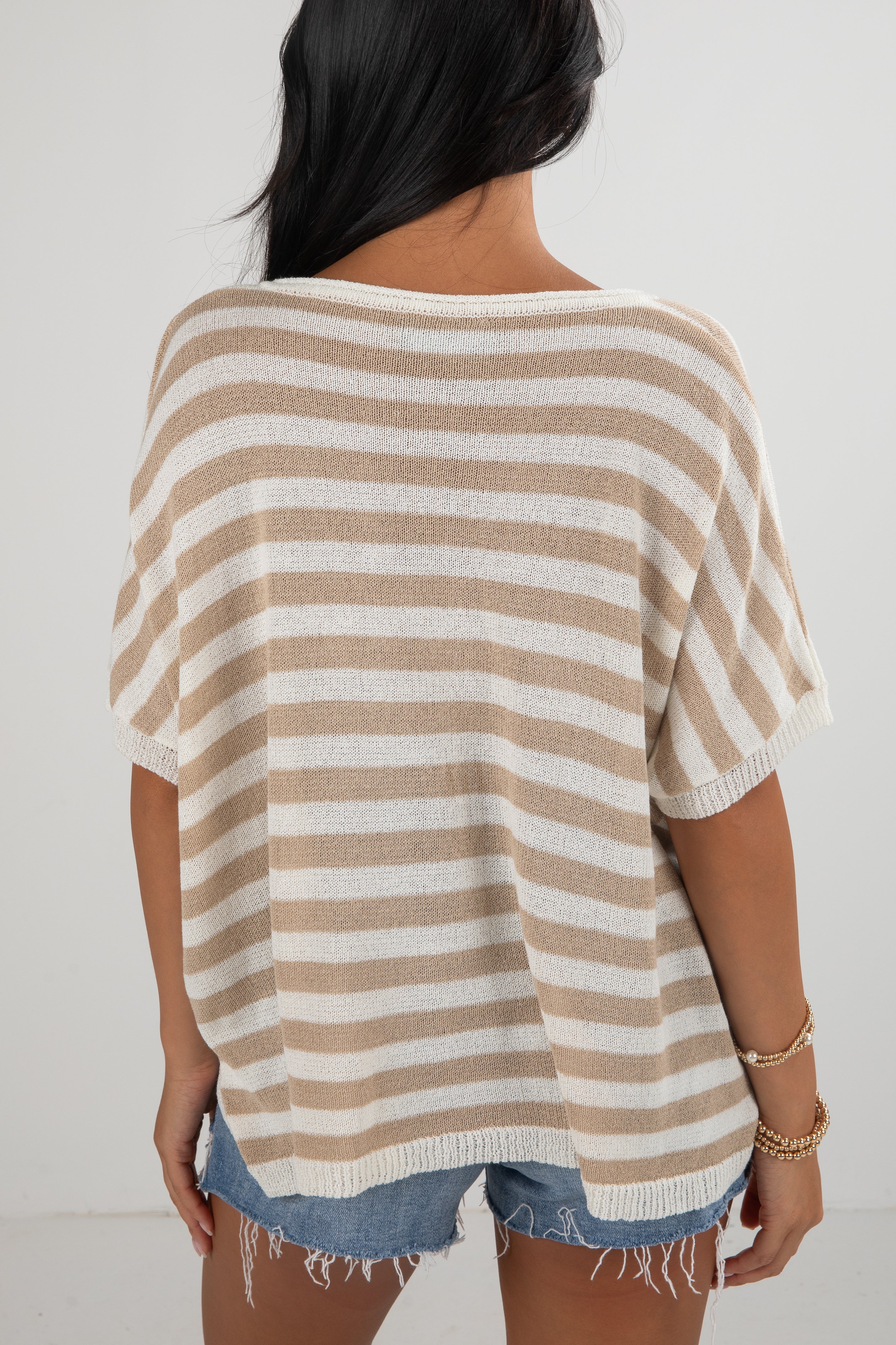 Woman wearing a beige and white striped sweater with denim shorts on a plain background