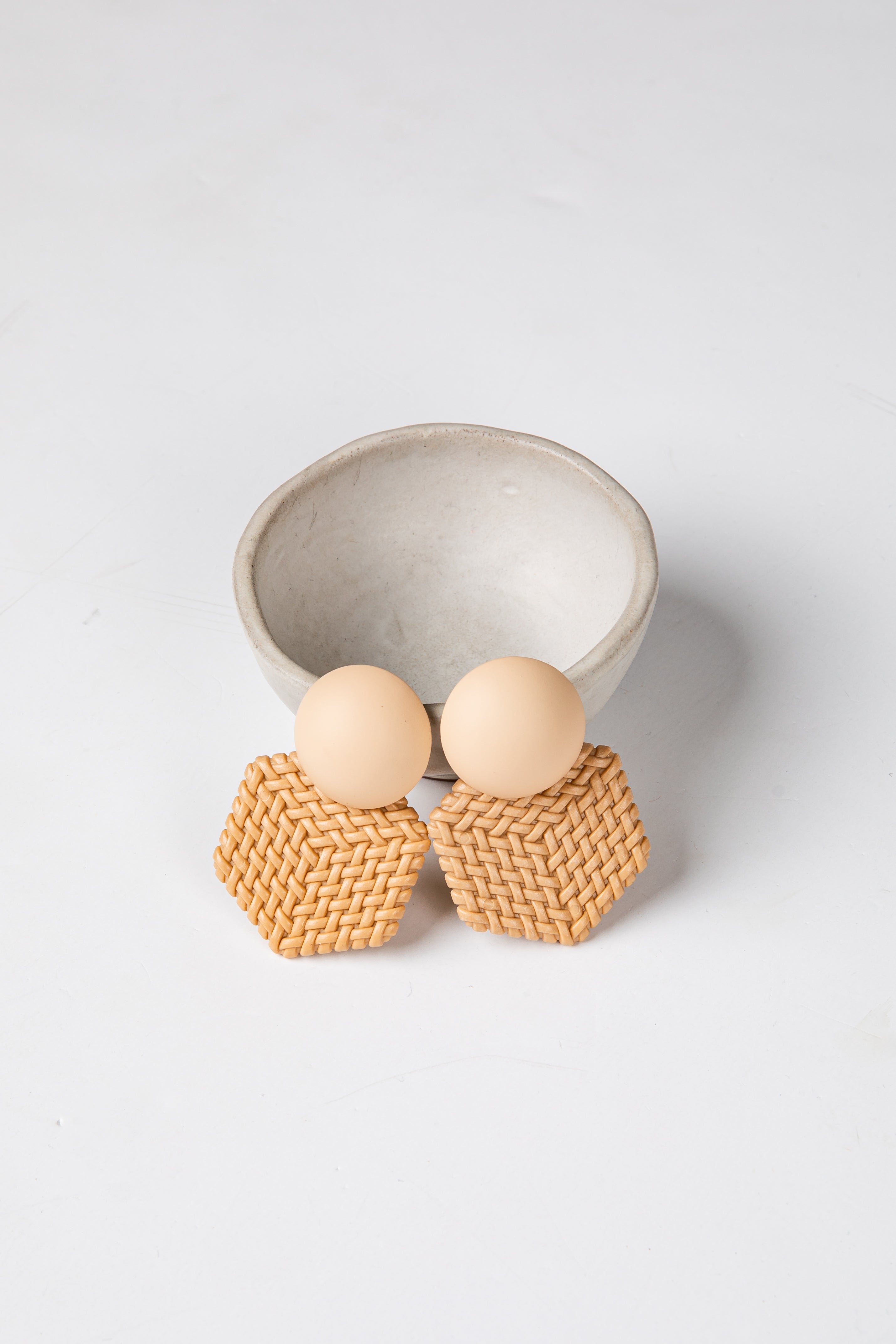 Pair of earrings with woven design and wooden beads on a light gray background