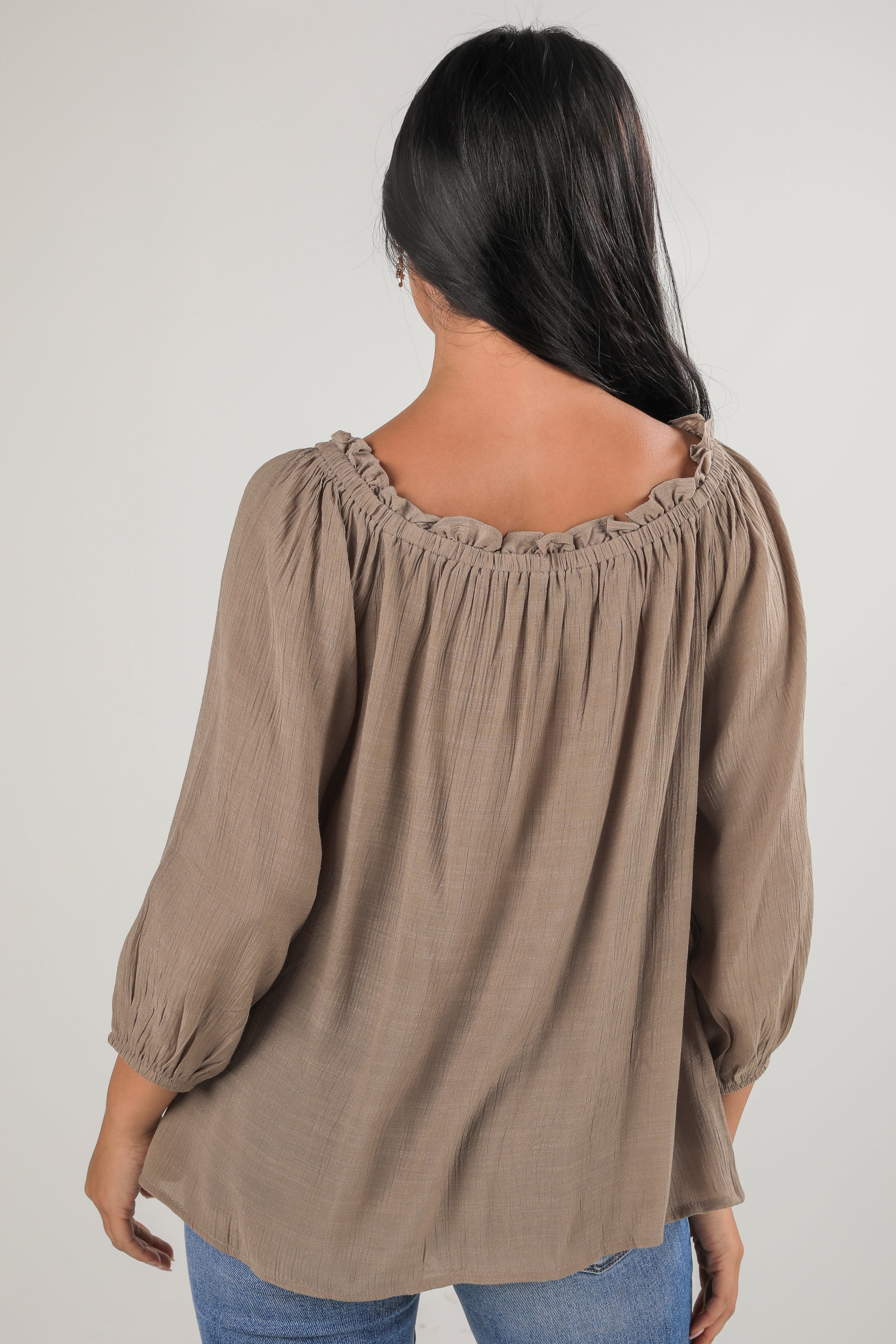 Woman wearing a brown blouse with long sleeves on a plain background