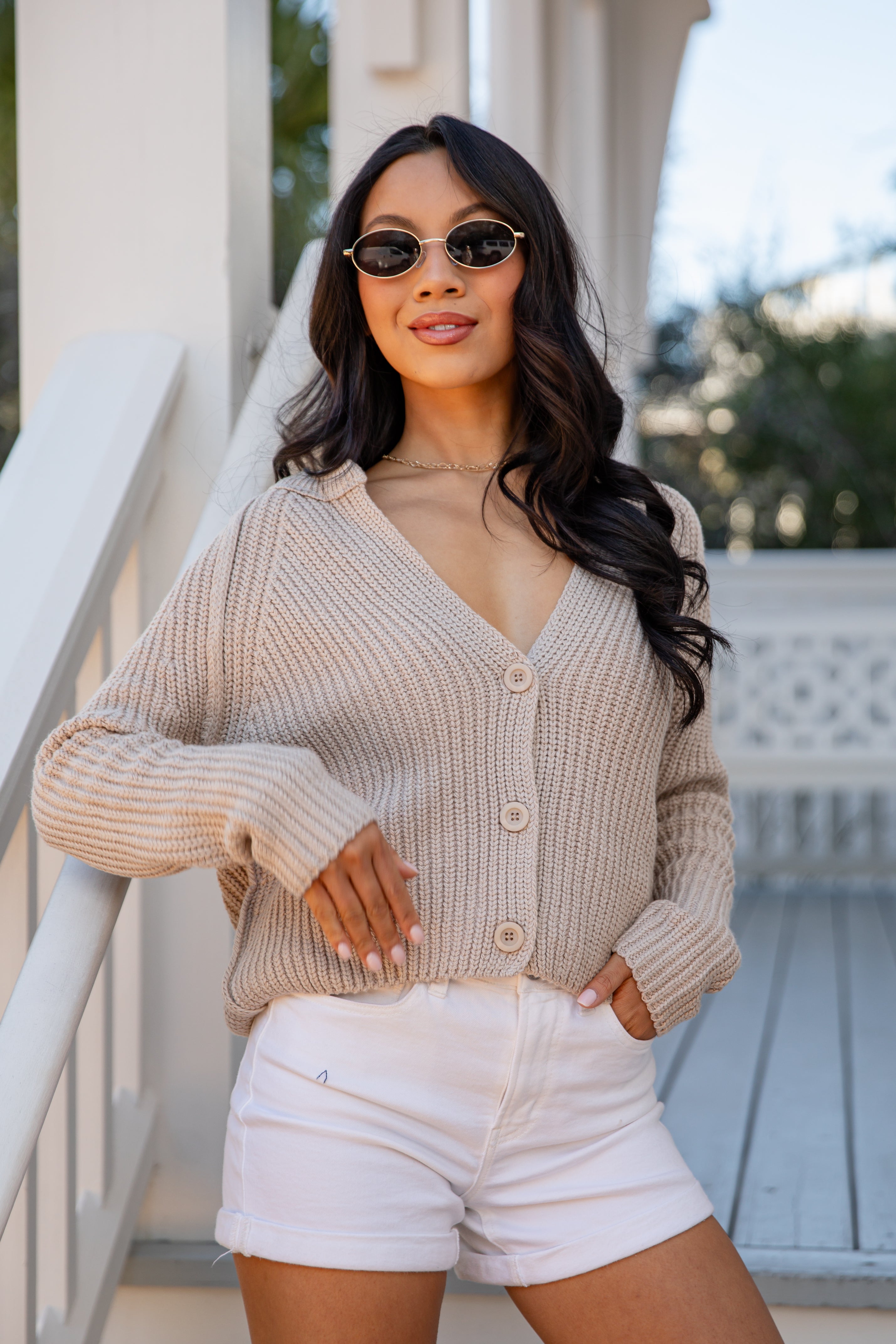 Woman wearing a beige cardigan and white shorts standing on a staircase.