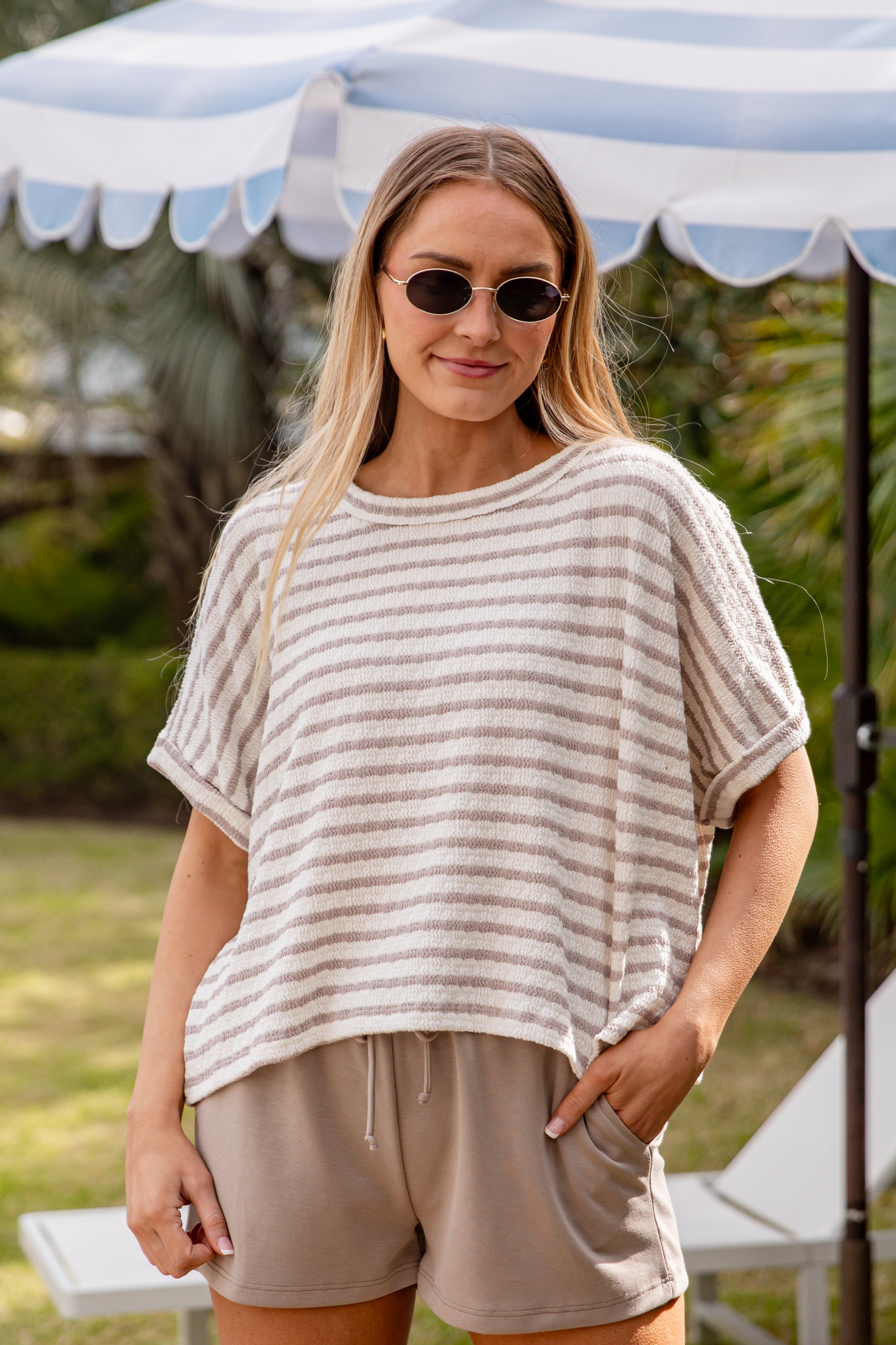 Woman wearing a striped shirt and shorts under a striped canopy.