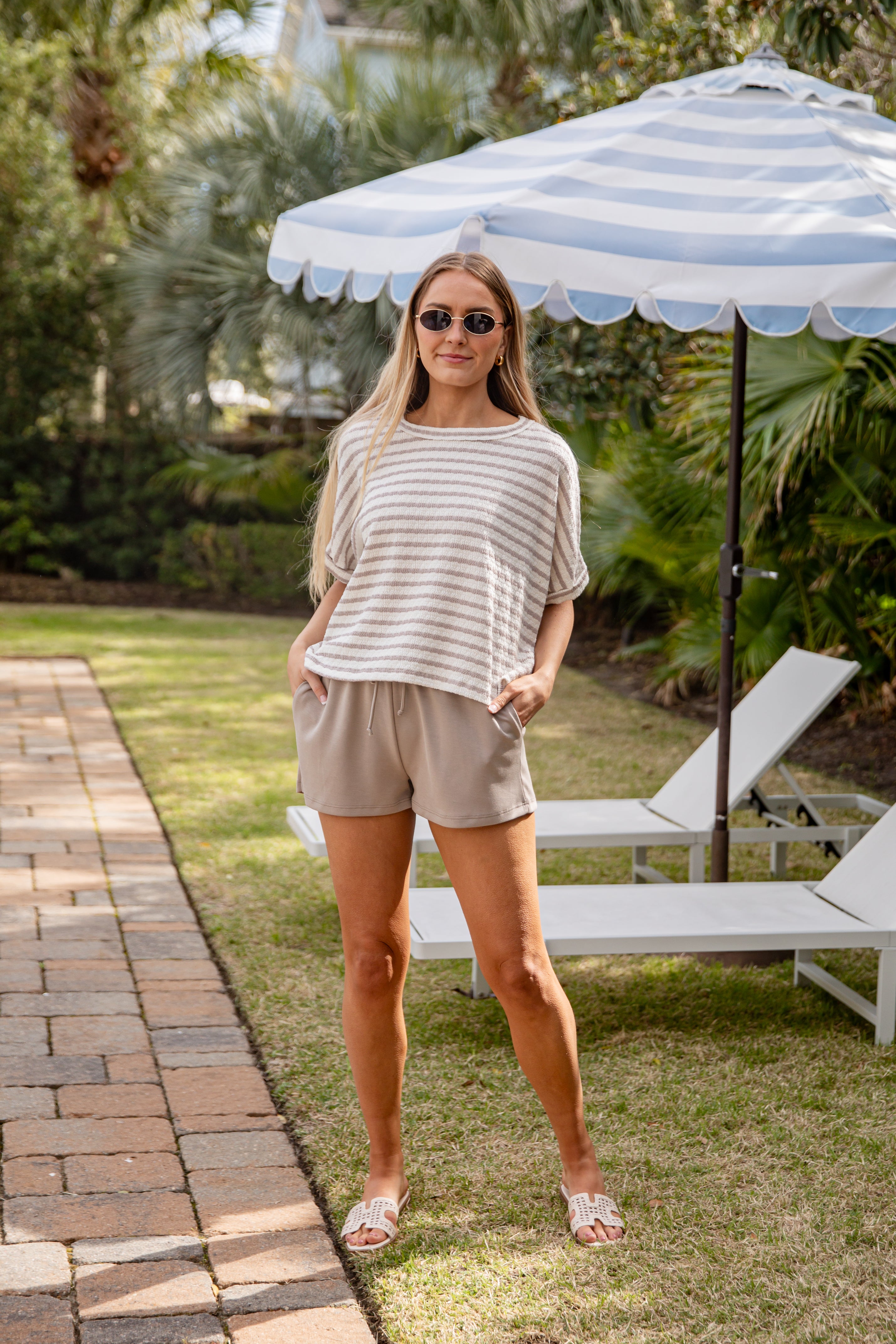Woman standing under a striped umbrella in a garden setting