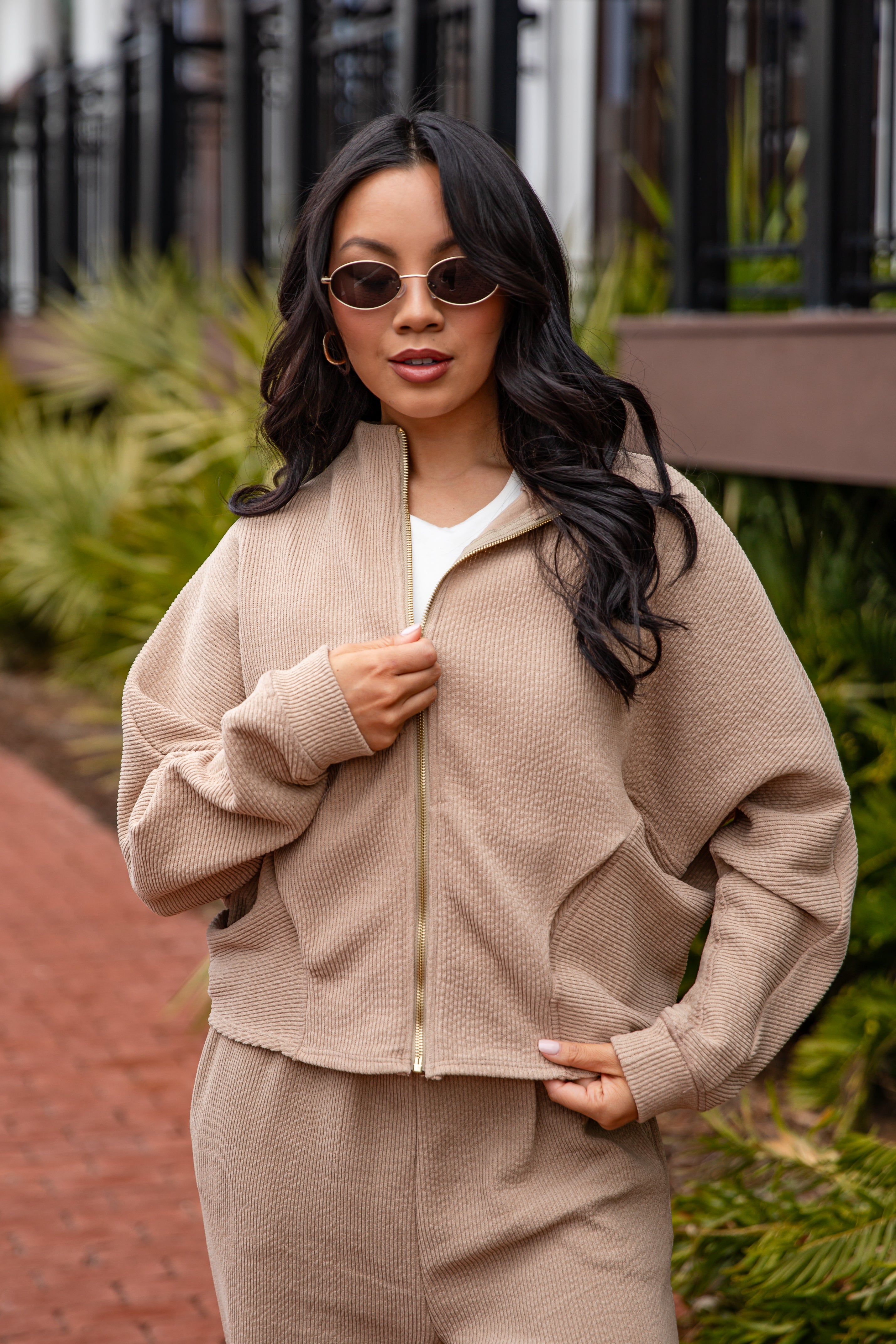 Woman wearing a beige tracksuit with sunglasses outdoors.